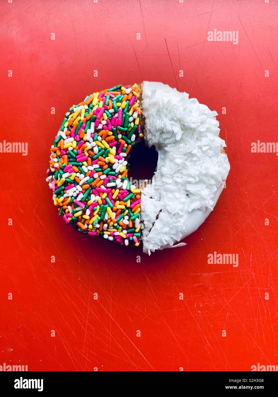 Half a colored sprinkle donut and half of a white coconut donut on a red background. - Smartphone Captured Stock Image
