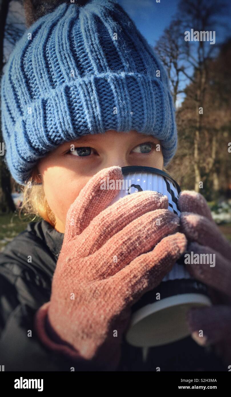 Young girl wearing woolly hat and gloves drinking a hot drink on a cold day Stock Photo