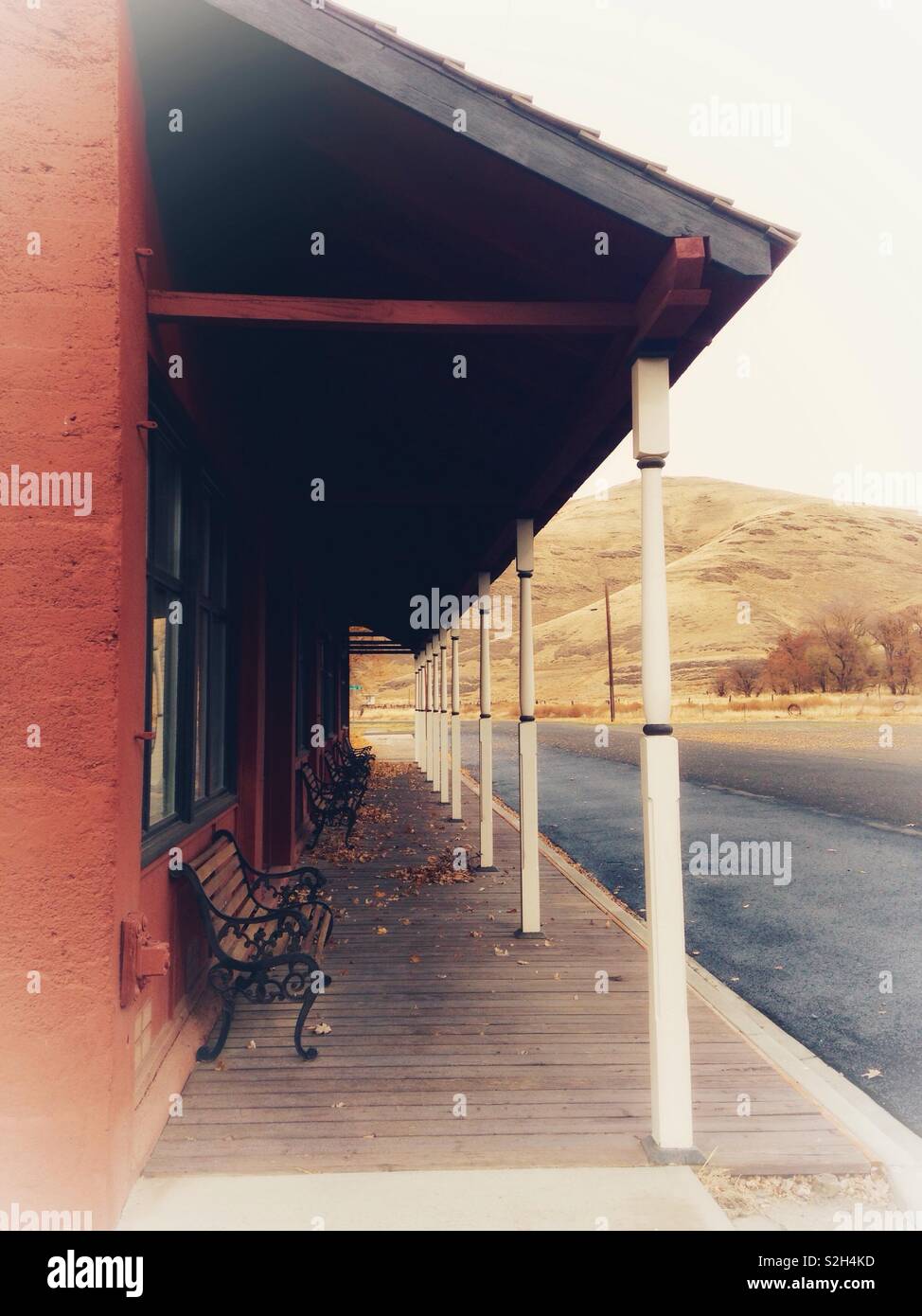 Pitched eave over wooden plank walkway in front of Old West type store, with November hillside in background - Smartphone Captured Stock Image