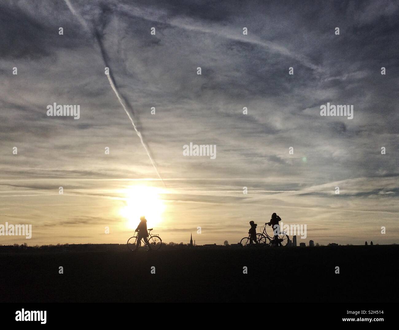 Cyclists are silhouetted against the setting sun as they wheel their bikes at Walthamstow Wetlands, London, UK. - Smartphone Captured Stock Image