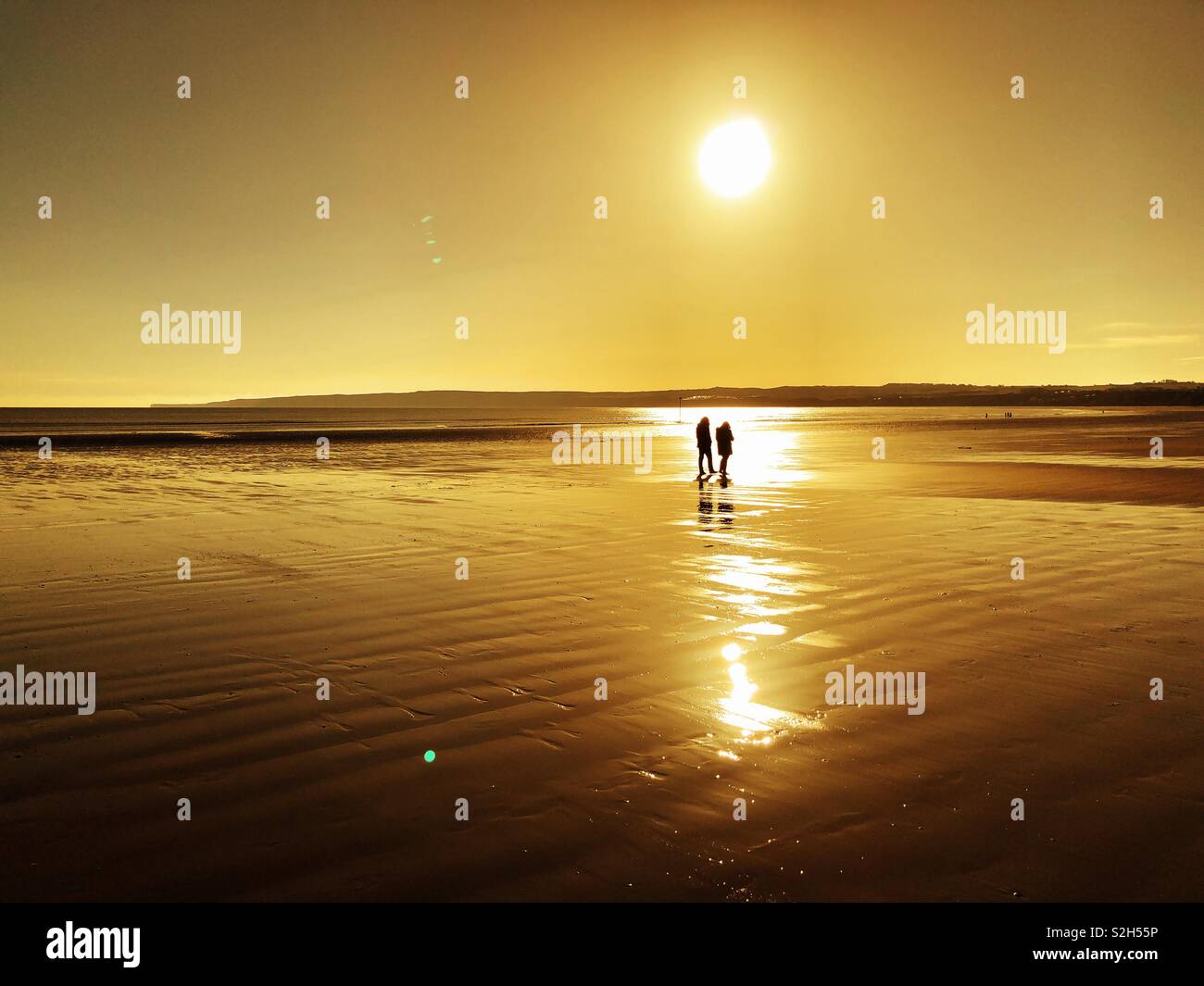 Silhouette of a couple walking along a wet beach in low winter sun - Smartphone Captured Stock Image
