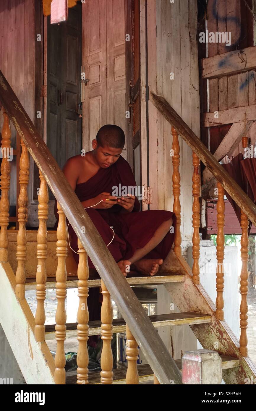 Young buddhist monk sitting on stairs and gaming on his mobile device Stock Photo