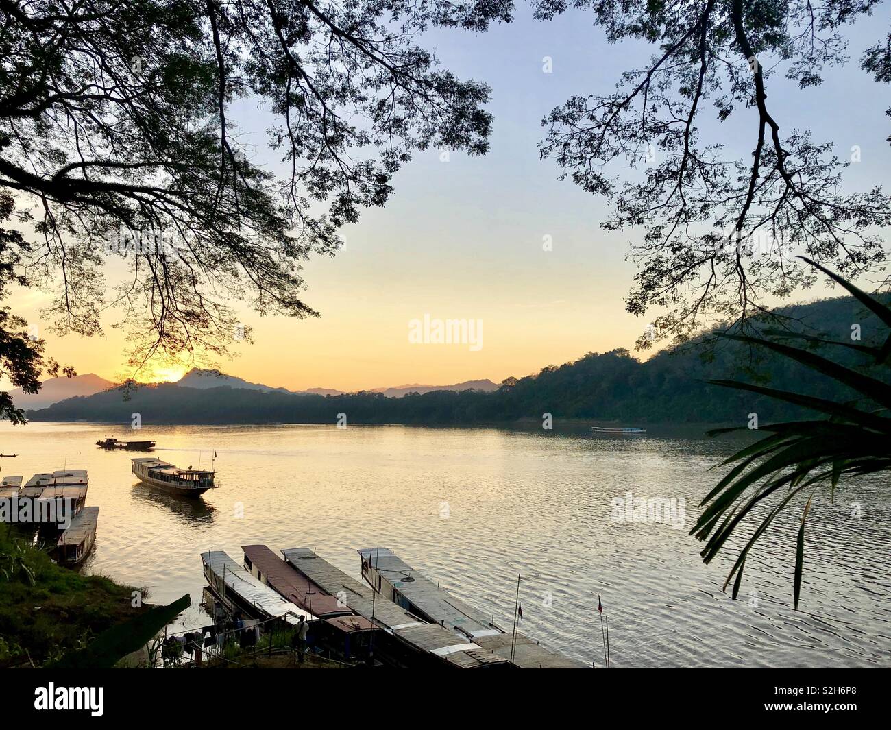 Boats on river Mekong at sunset under orange sky in Luang Prabang - Smartphone Captured Stock Image