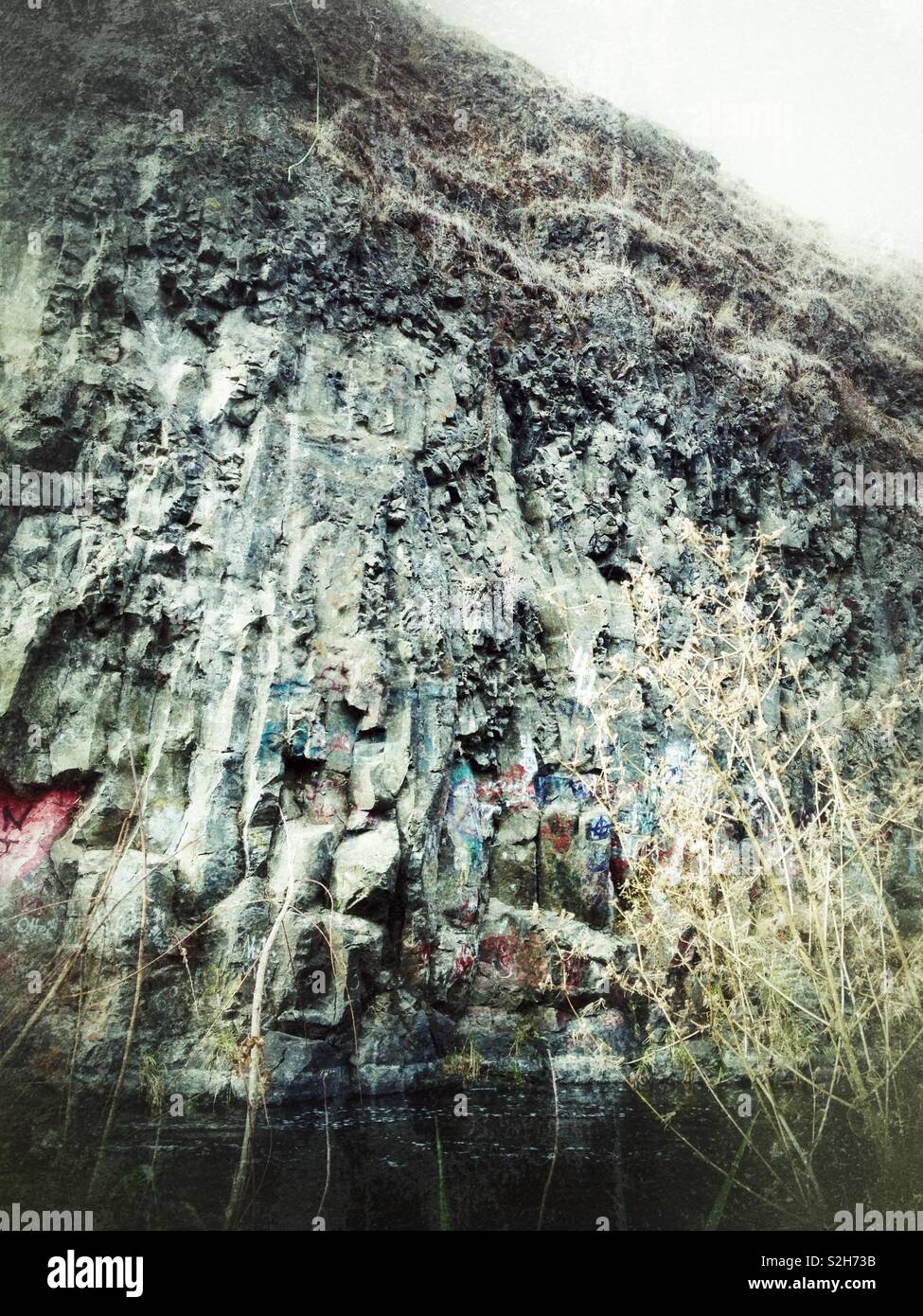 Rock wall covered with graffiti beside stream - Smartphone Captured Stock Image