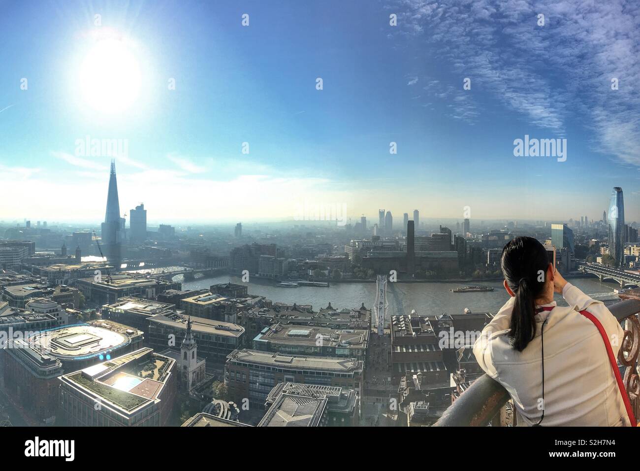 Woman taking photo with smartphone of London skyline from the top of St Paul’s cathedral. View showing the Thames, Shard, Tate Modern and Millennium Bridge - Smartphone Captured Stock Image