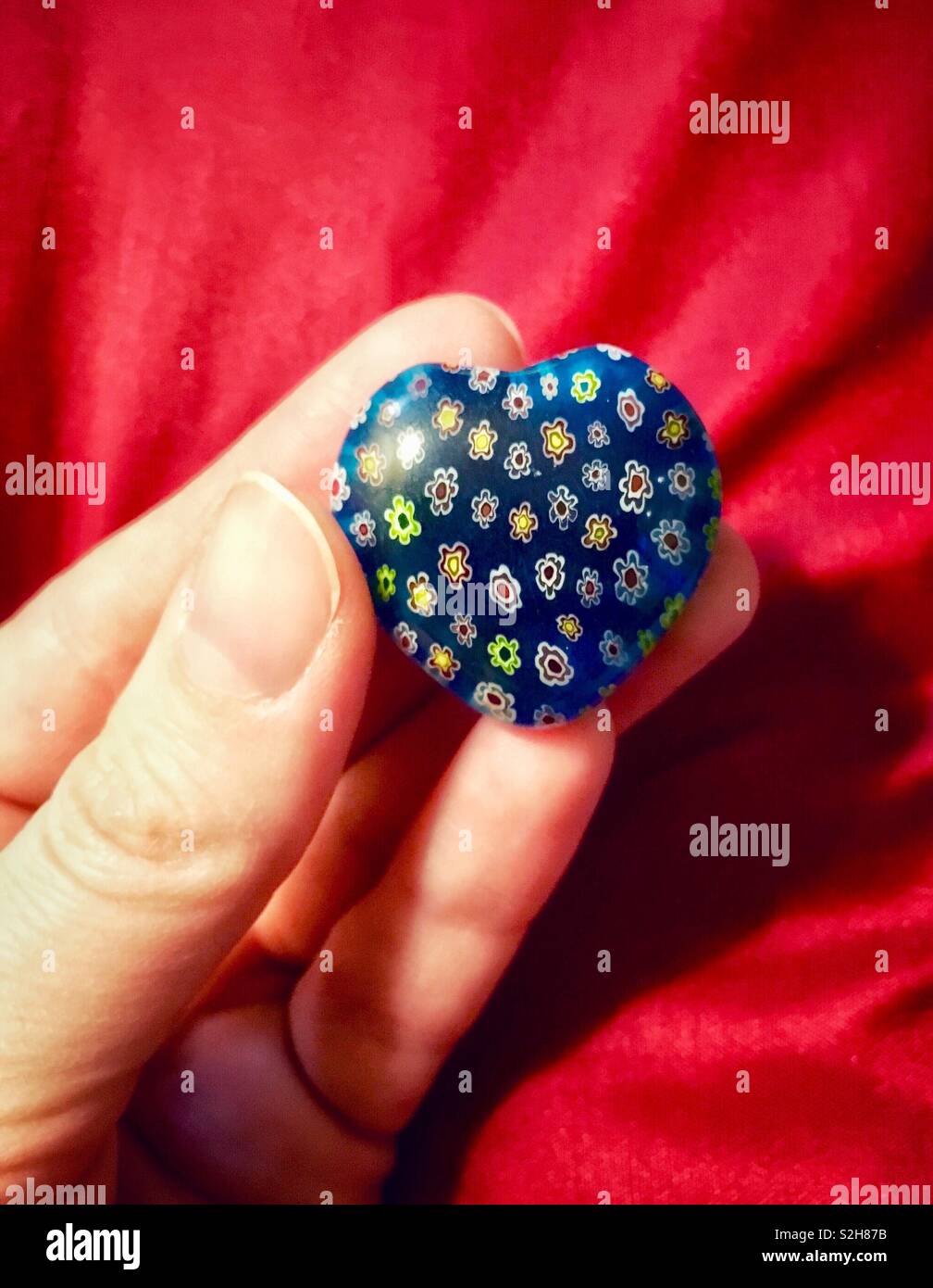 Woman holding blue glass heart with tiny colorful flowers against red background for Valentine’s Day - Smartphone Captured Stock Image