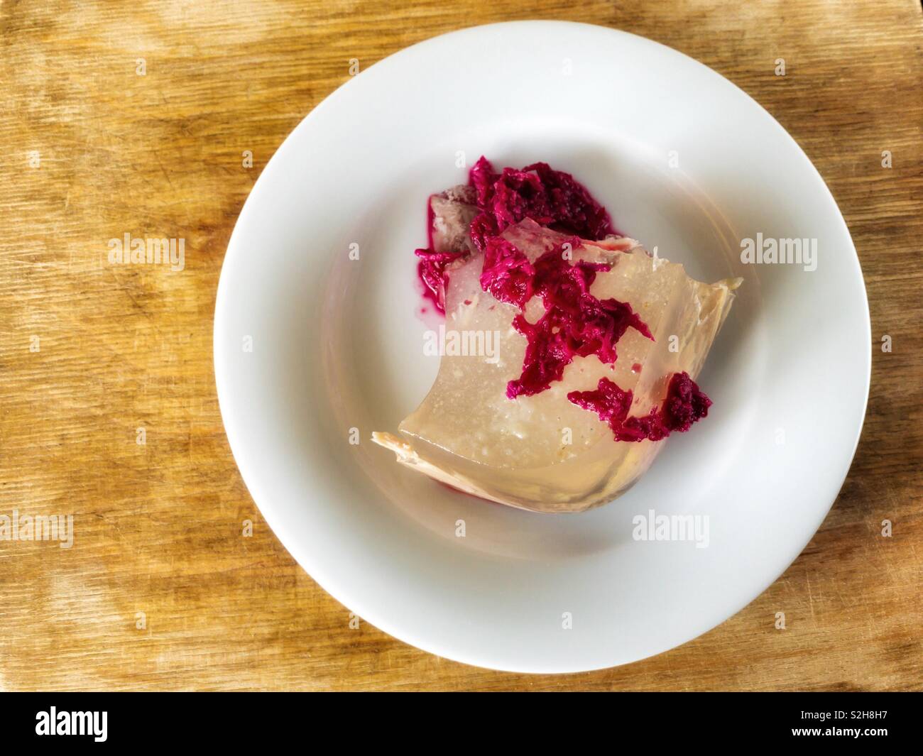 Plate with Ukrainian aspic flavored with horse-radish pickled in beetroot juice standing on wooden surface Stock Photo