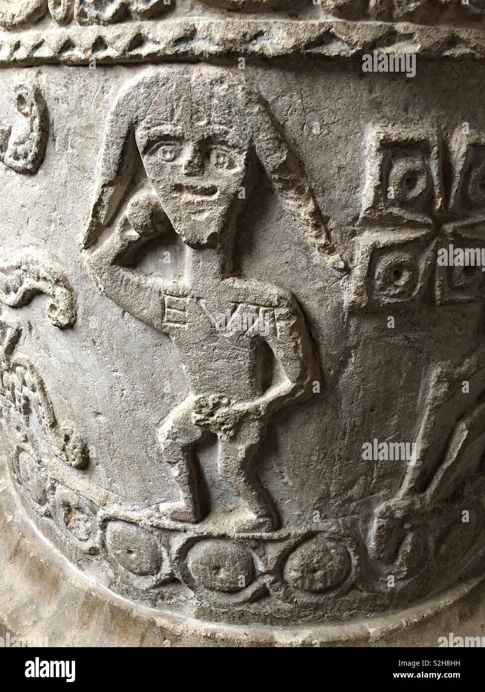 A stunning primitive Norman sculpture of Eve after the expulsion from the Garden of Eden, on an Oxfordshire font with her name ‘Eva’ inscribed on her. Stock Photo