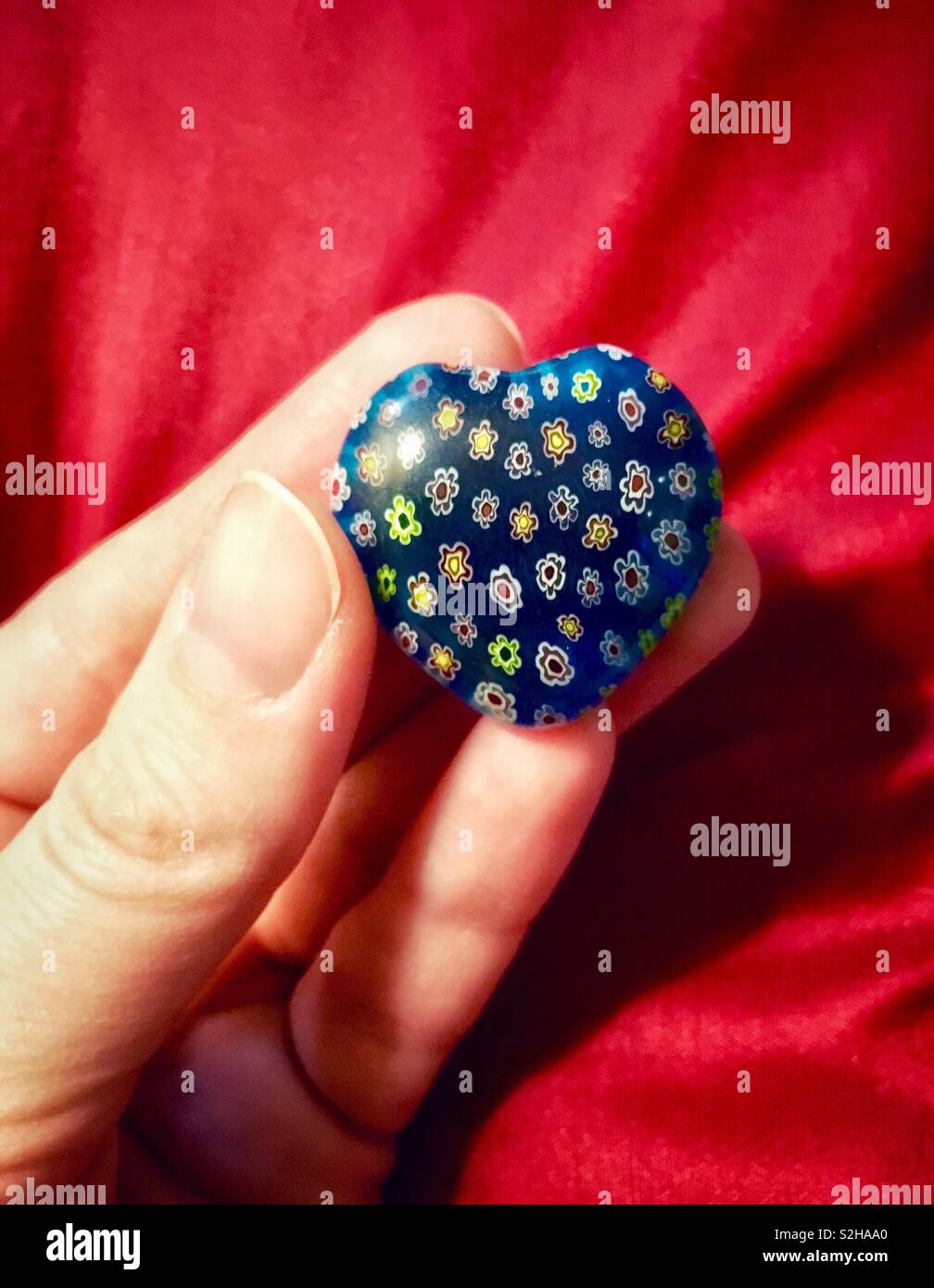 Woman holding blue glass heart with tiny colorful flowers against red background for Valentine’s Day - Smartphone Captured Stock Image