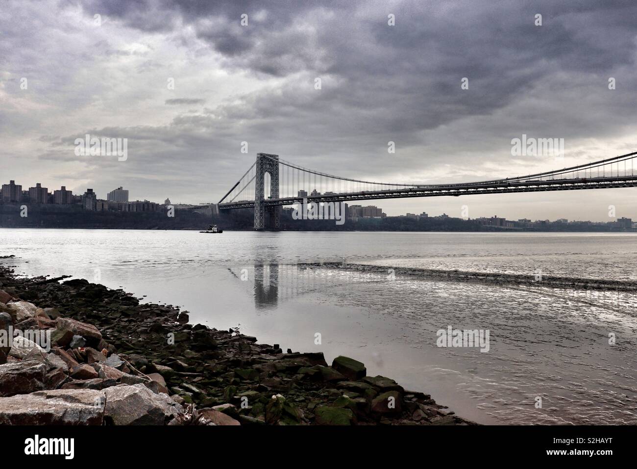 George Washington Bridge casting a reflection on an overcast day with small boat passing underneath Stock Photo