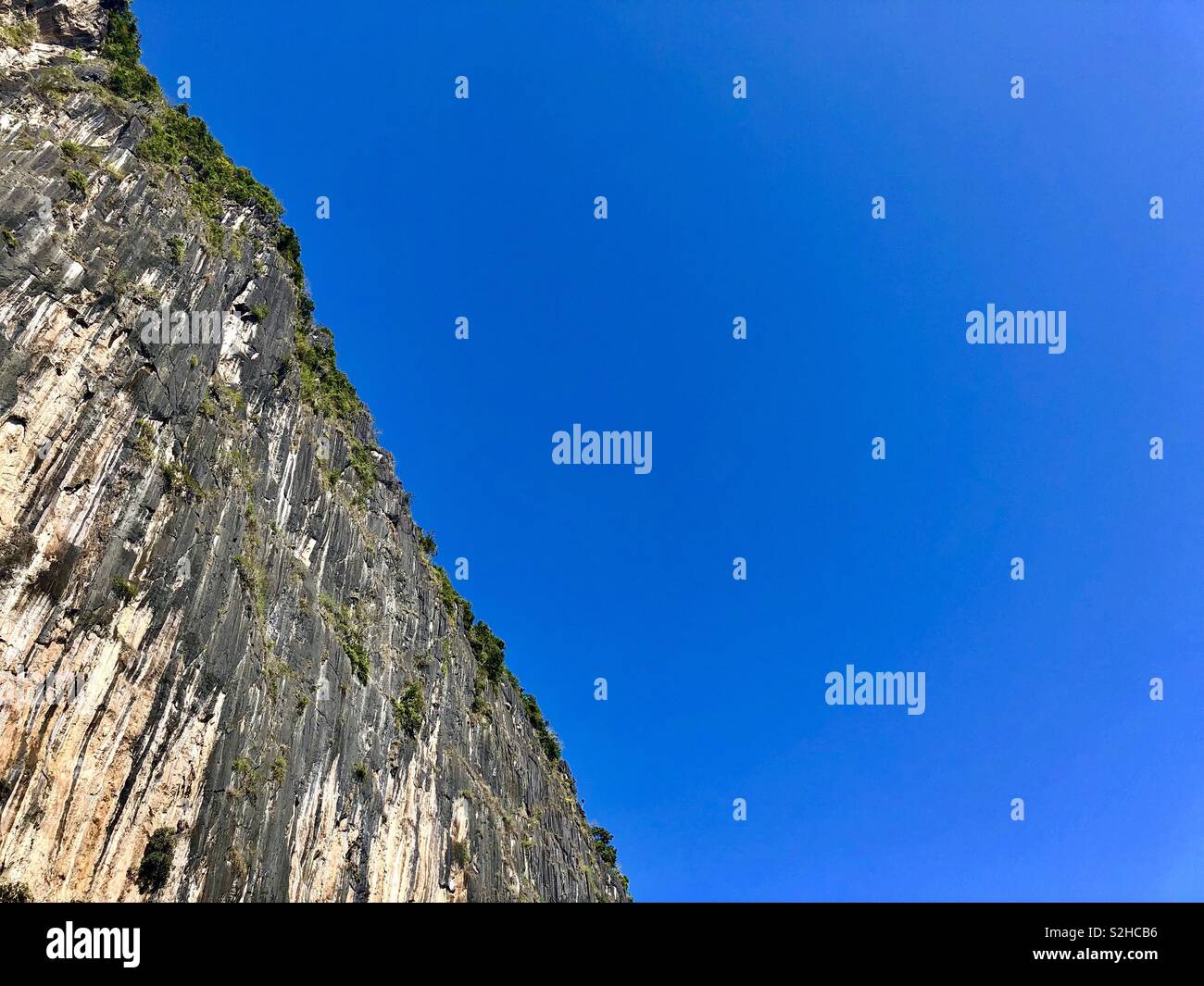 Low angle view looking up cliff under clear bright blue sky - Smartphone Captured Stock Image