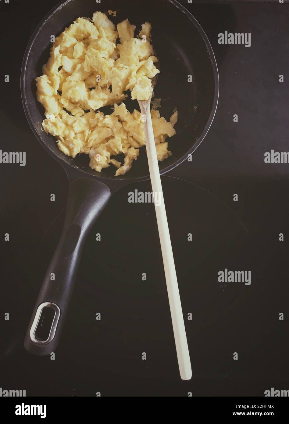 Scrambled eggs in black frying pan with wooden spoon on black stovetop - Smartphone Captured Stock Image