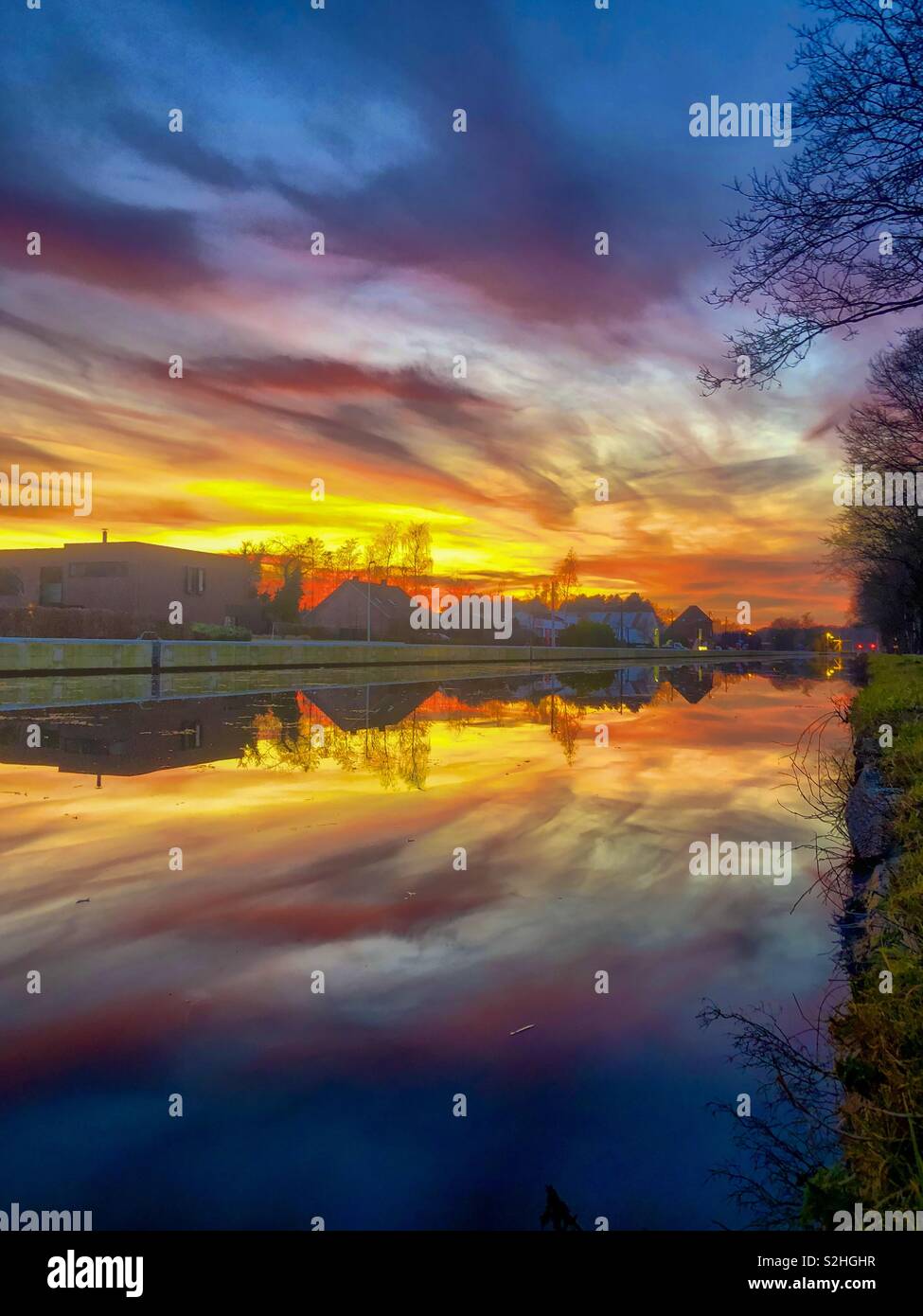 Dramatic and colorful sunset over the river with the gold, yellow, orange, red, purple and blue colors of the sky and the Clouds reflected in the water - Smartphone Captured Stock Image