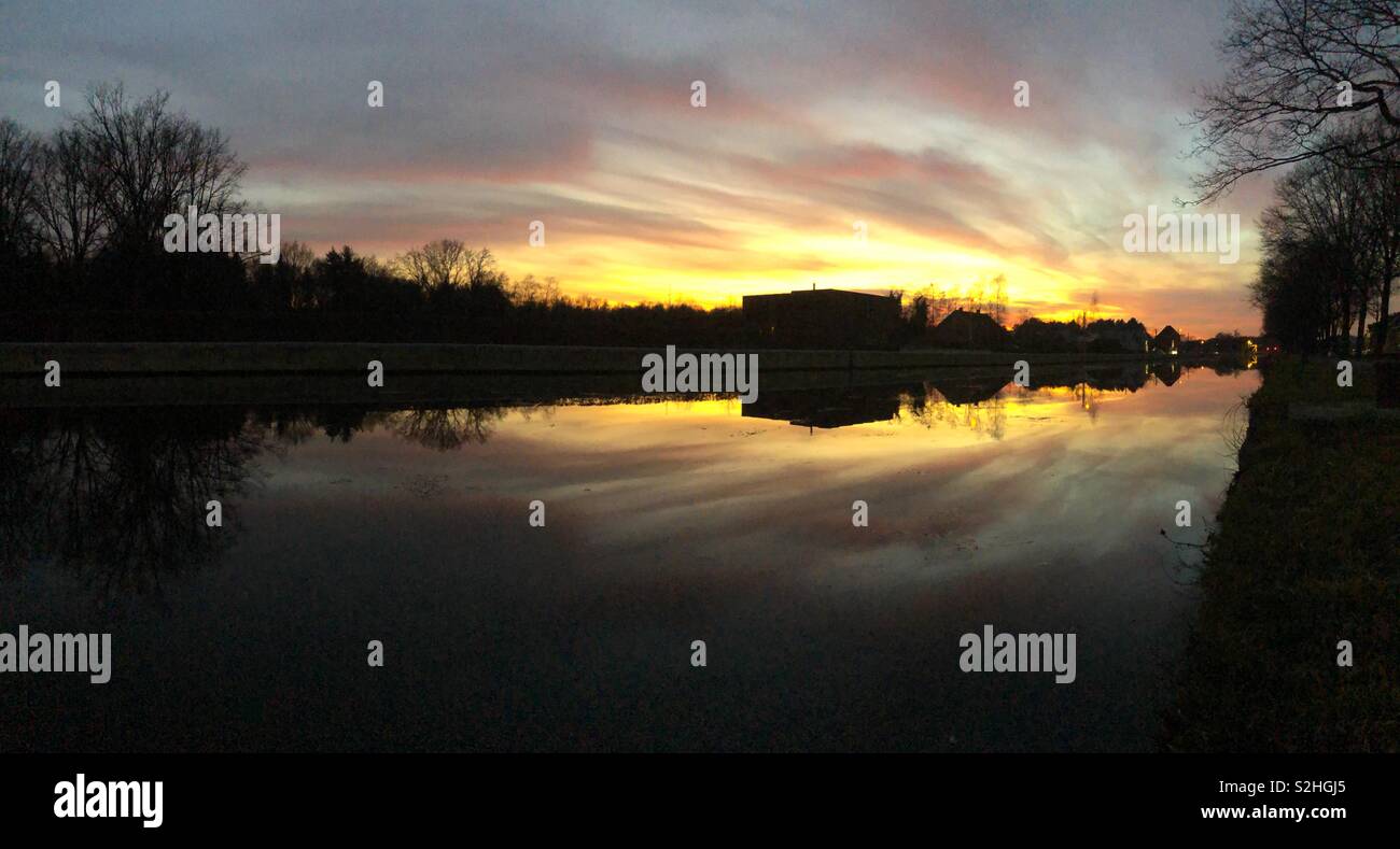 Dramatic and colorful sunset over the river with the gold, yellow, orange, red, purple and blue colors of the sky and the Clouds reflected in the water - Smartphone Captured Stock Image