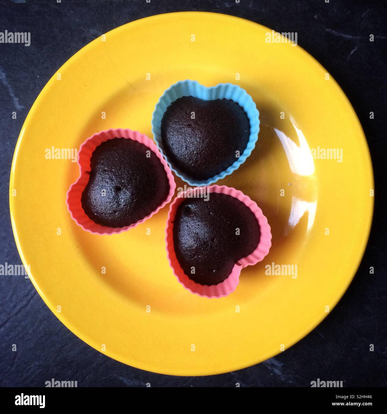 Three heart shaped chocolate cupcakes on a bright yellow plate Stock Photo