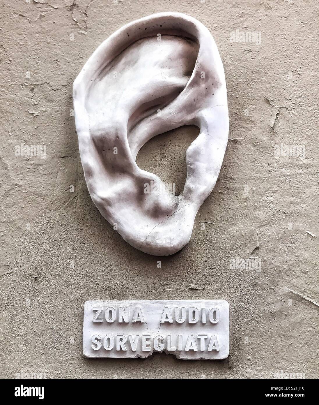 Zona audio sorvegliata, sculpture of an ear affixed to a wall to warm people that the area is under audio surveillance, Milan , Italy - Smartphone Captured Stock Image