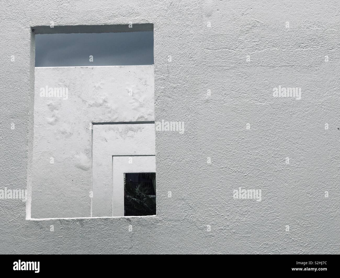 A rectangular opening in a white wall looks onto the same opening in the wall behind, repeated three times. - Smartphone Captured Stock Image