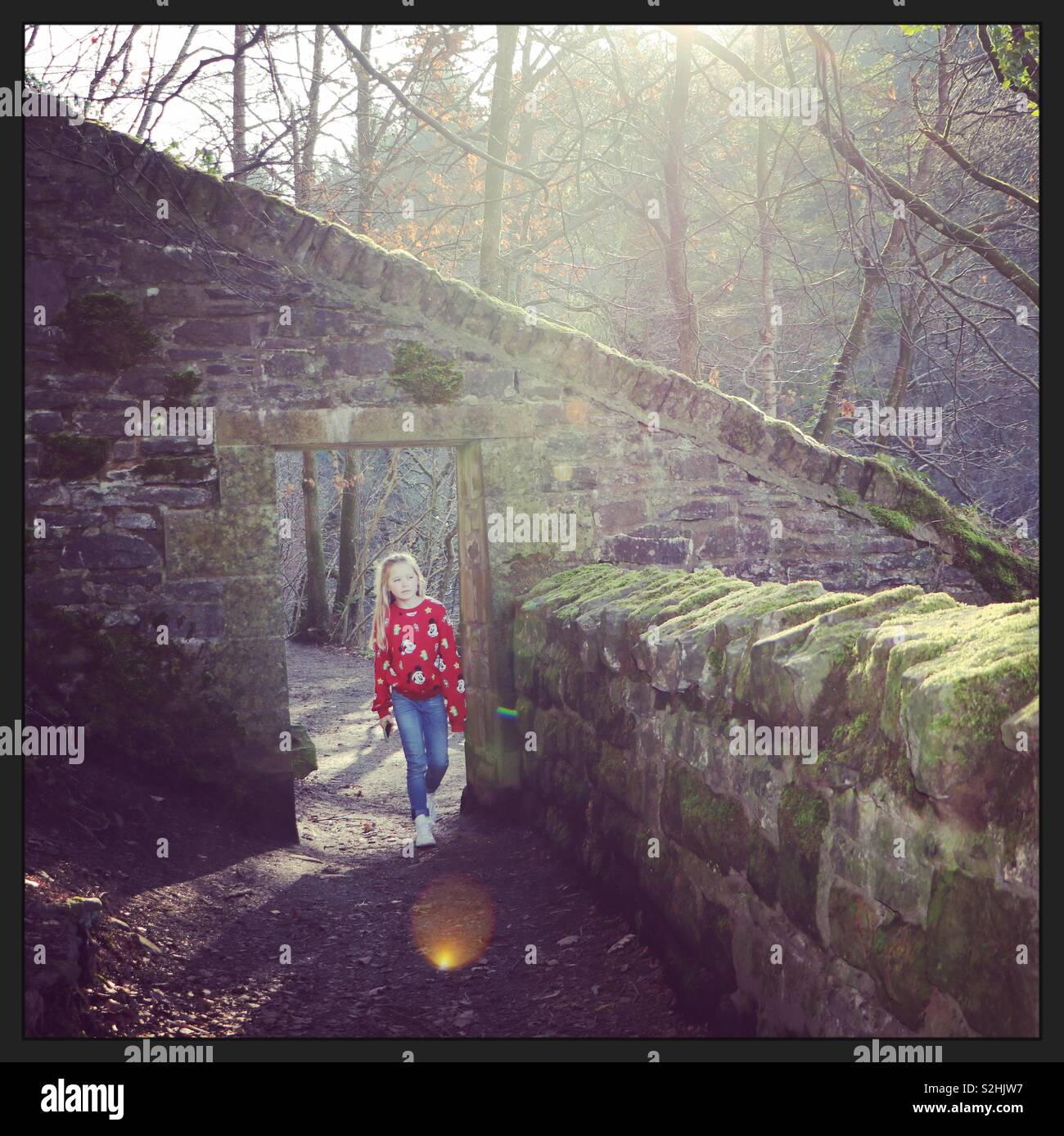 Girl walking through stone doorway in sunlight Stock Photo