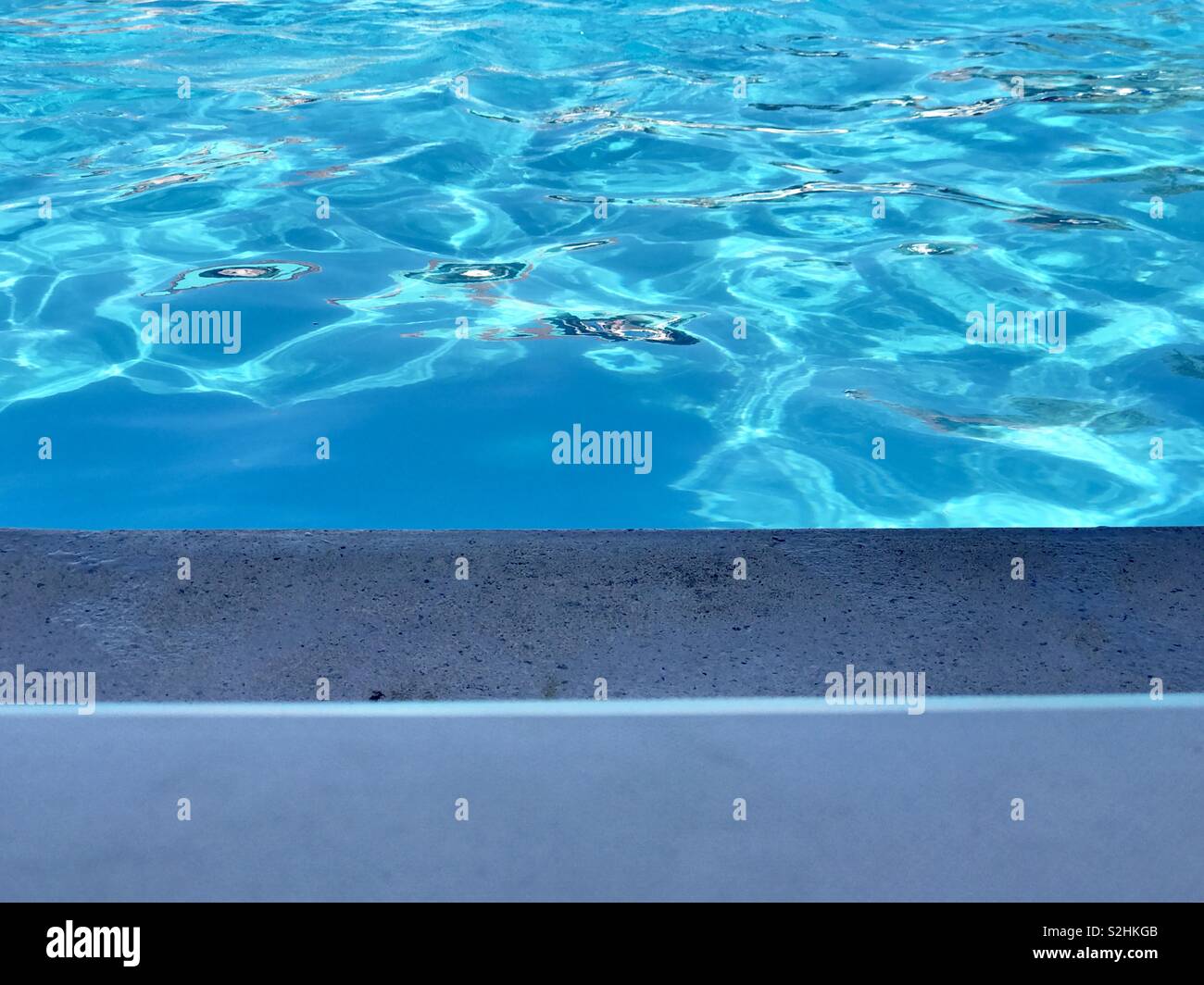 The edge of a lounge chair, the edge of a pool, and the pool water. - Smartphone Captured Stock Image