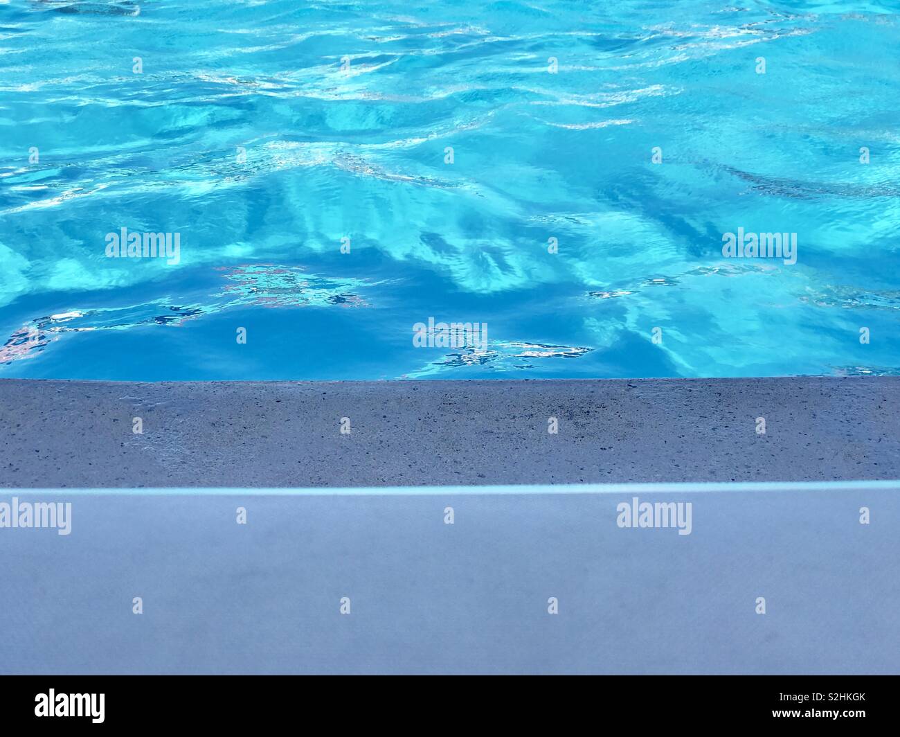 The edge of a lounge chair, the edge of a pool, and the pool water. - Smartphone Captured Stock Image