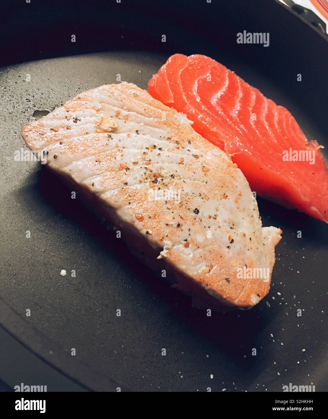 Fresh tuna steaks being seared in a hot skillet on a stove top, USA - Smartphone Captured Stock Image