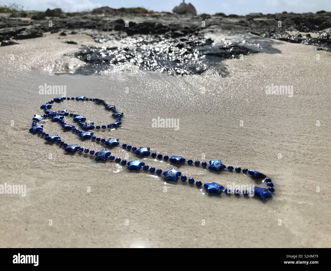 A necklace with blue stars lies on a beach. - Smartphone Captured Stock Image