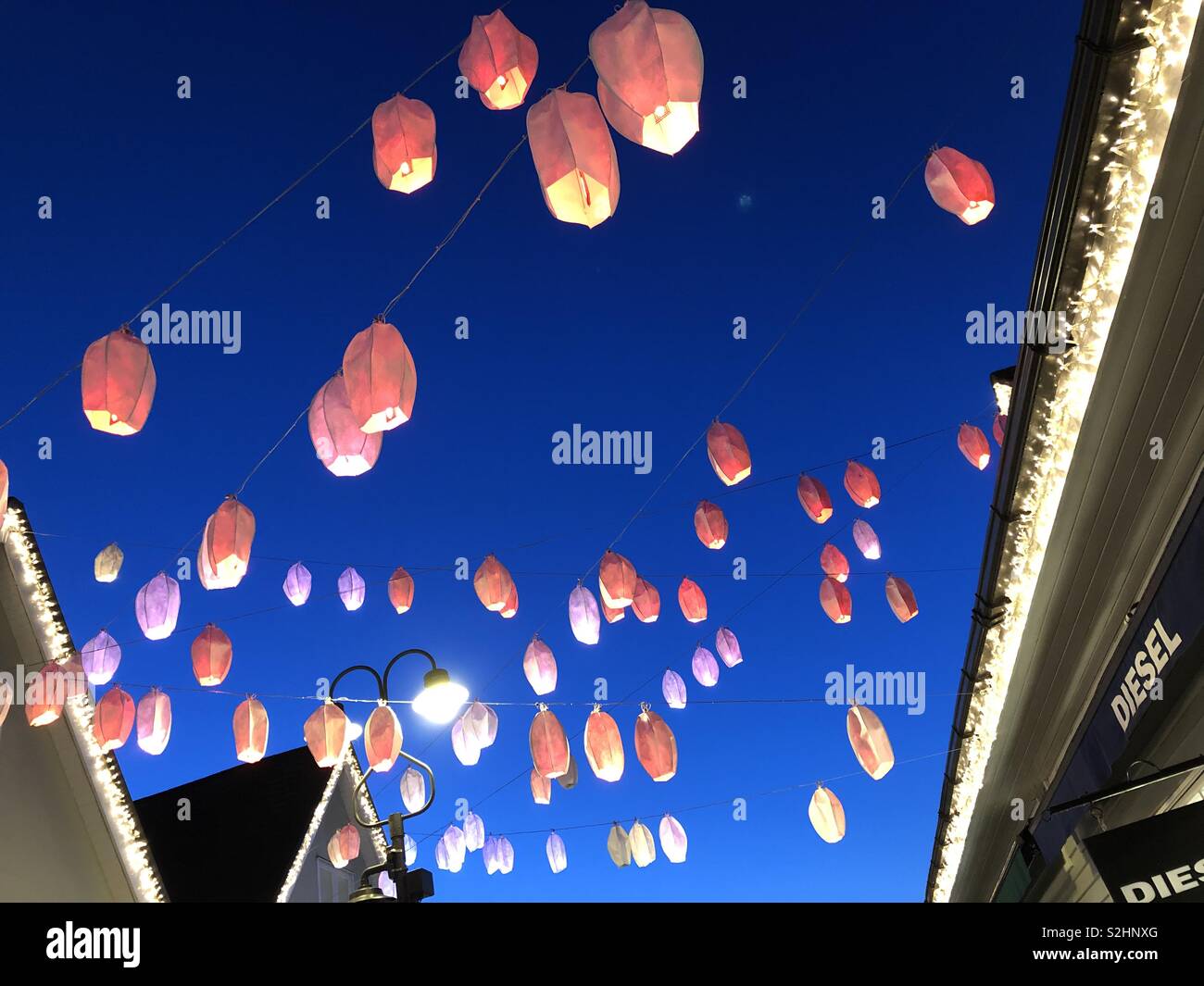 Beautiful Orange and Mauve Chinese lanterns suspended on crisscrossing wires contrasted against a deep blue sunset sky to celebrate the Chinese New Year at Bicester Village England. Stock Photo