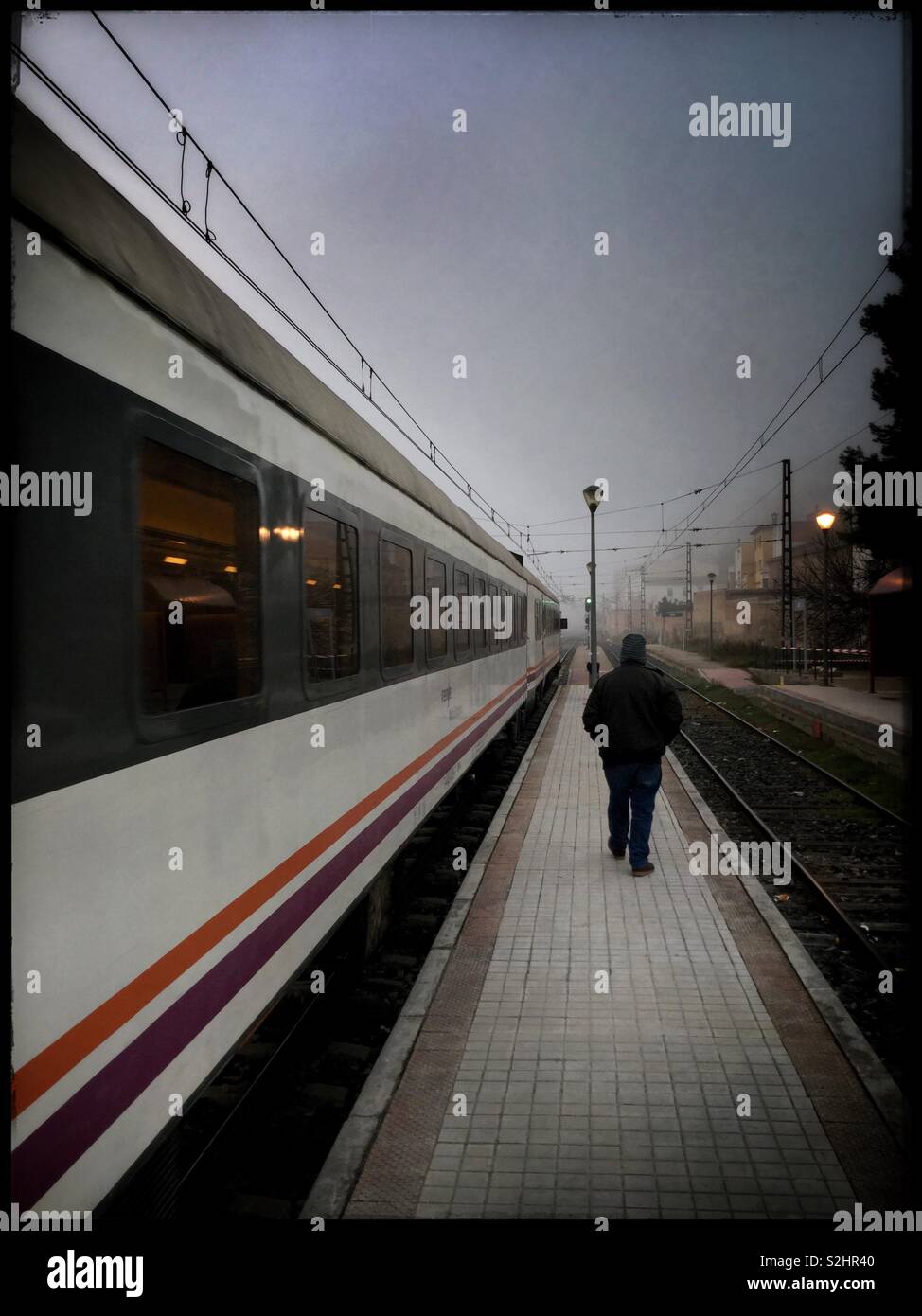 A train leaves the station at Ascó as a man walks by, Catalonia, Spain. - Smartphone Captured Stock Image