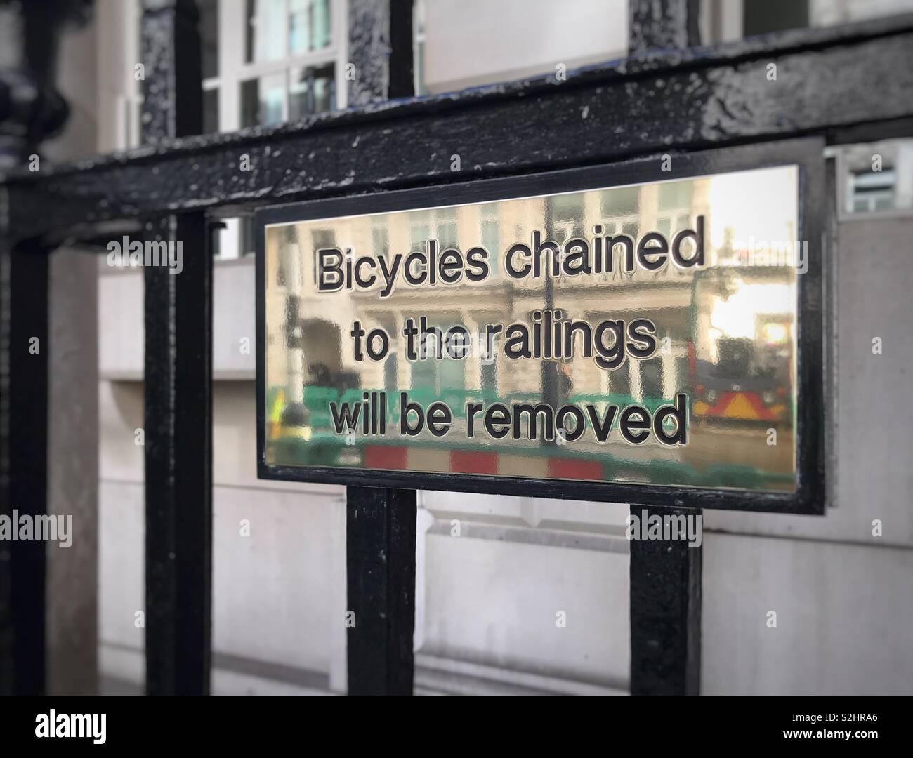 Notice on a brass plate attached to metal railings warning the public that any bicycles chained to the railings will be removed. Stock Photo