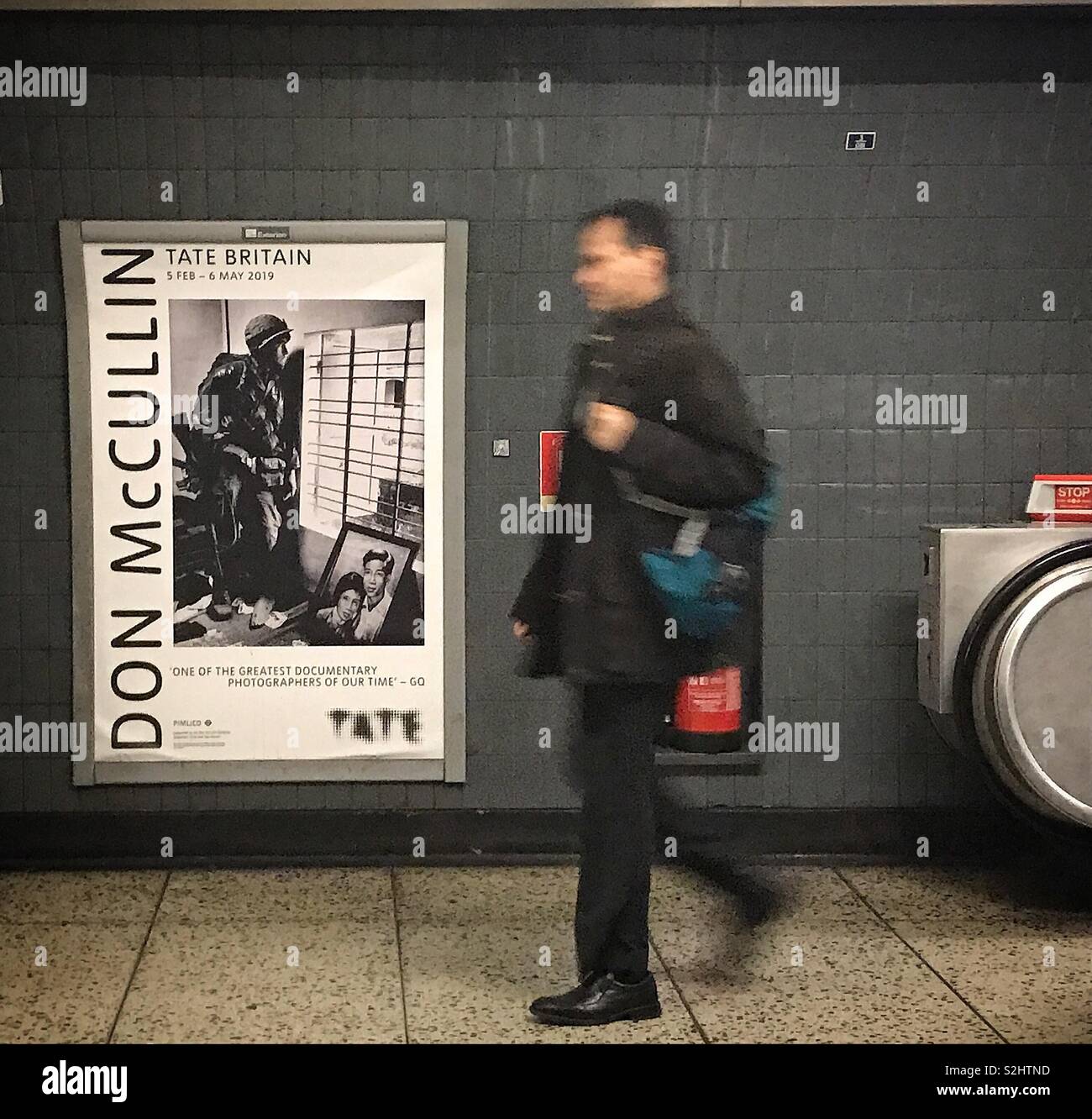 Man walking past an advertisement promoting the exhibition of photographs by Don McCullin at London’s Tate Britain art gallery - Smartphone Captured Stock Image