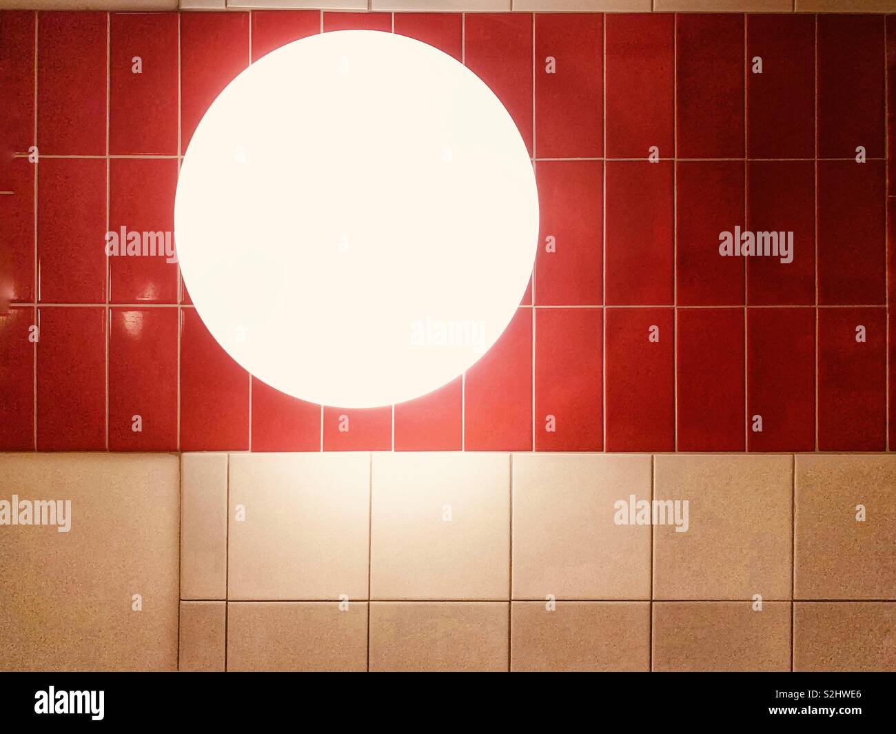 Round glowing light against a red and white tiled wall - Smartphone Captured Stock Image