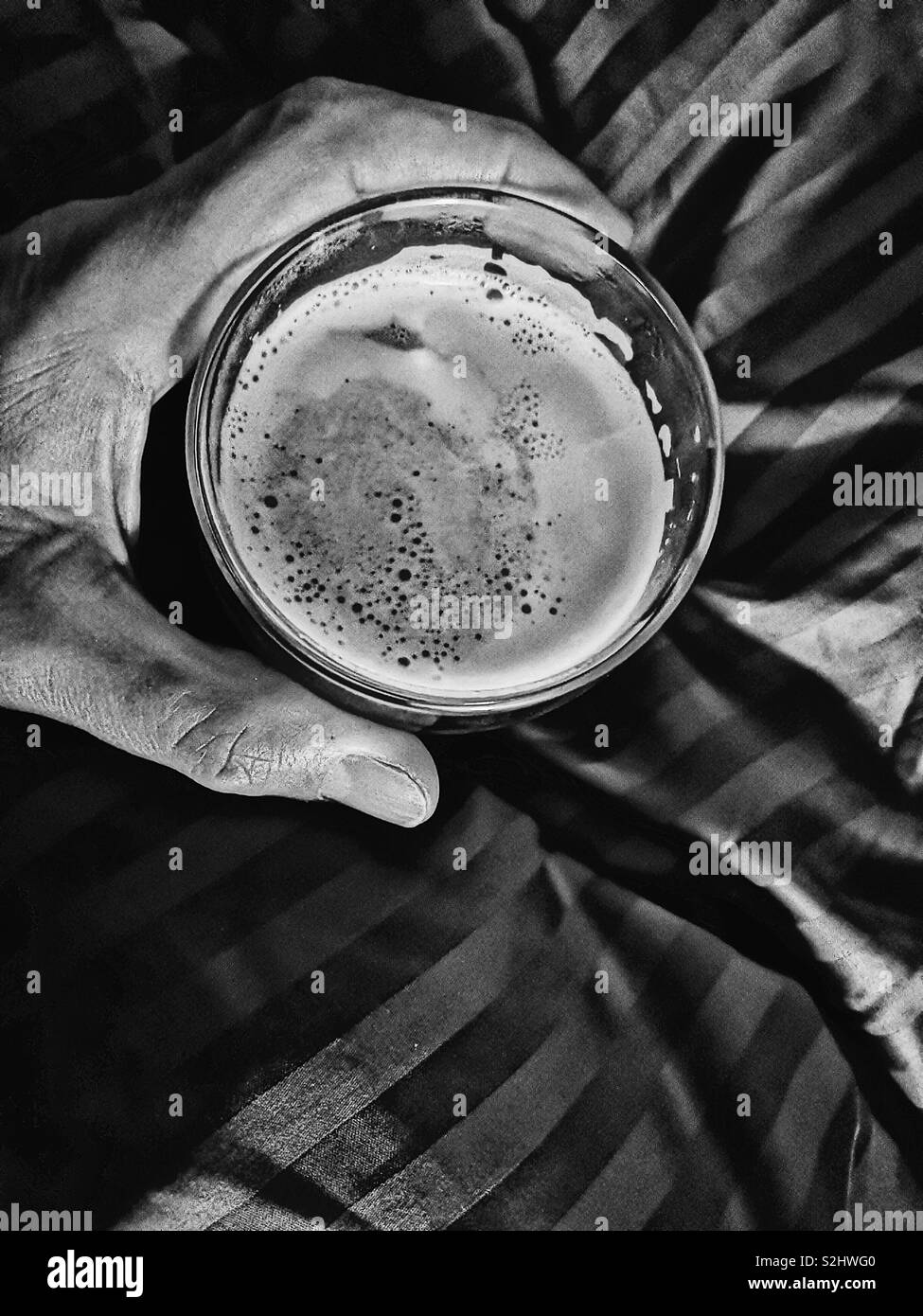 Elevated view of man’s hand holding glass of cafe latte in bed - Smartphone Captured Stock Image