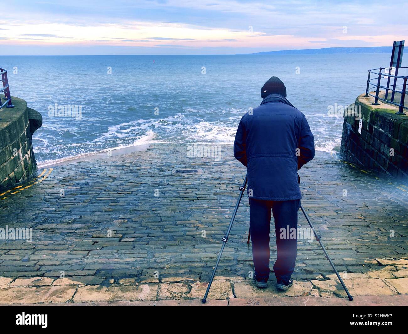 Photographer setting up a long exposure shot as the waves roll down the slipway - back view Stock Photo