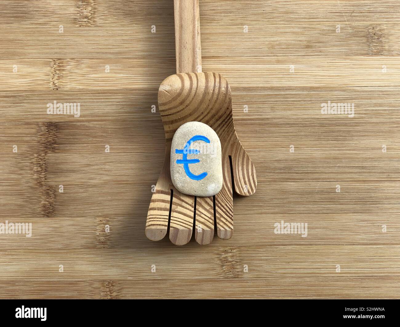 Need more euro, conceptual composition with a wooden hand and the symbol of euro carved on a stone - Smartphone Captured Stock Image