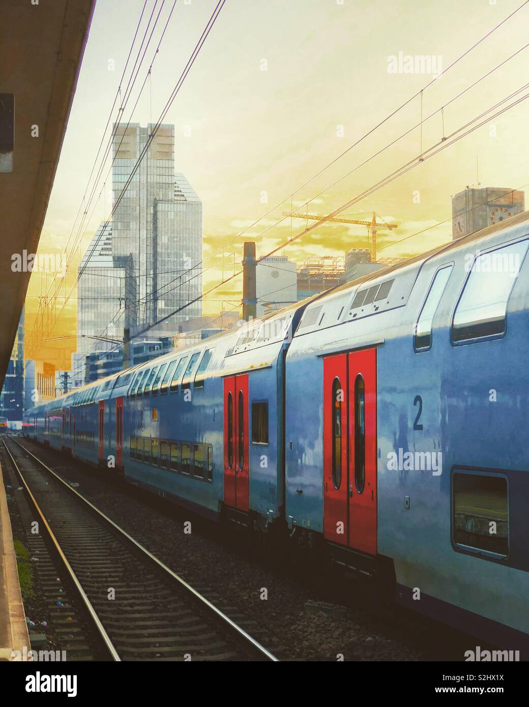 Train in the railway station of a modern city under a surreal Golden sky with the skyscraper office towers of the business district in the distance - Smartphone Captured Stock Image