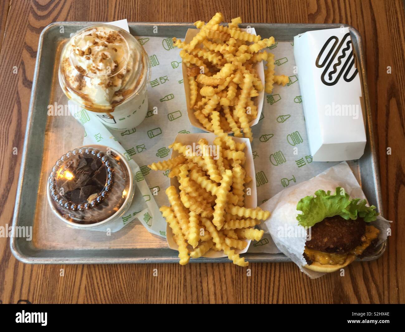 A tray of food from the Shake Shack. Apple pie milkshake with a chocolate brownie concrete ice cream. Crinkle cut chips a stack burger and a hotdog. Stock Photo