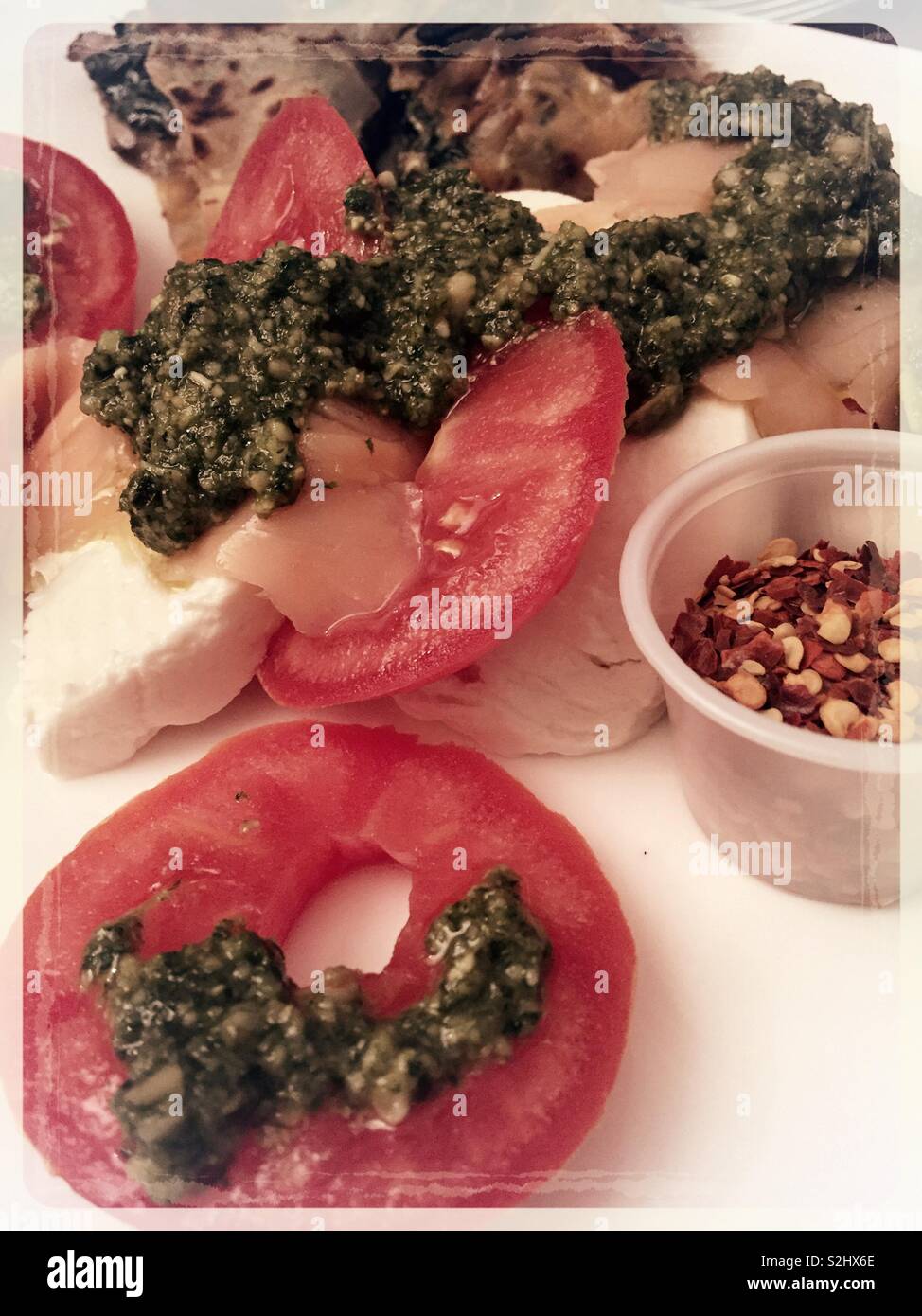 Close up of tomato, mozzarella, smoked salmon and pesto with a container of red pepper flakes Stock Photo