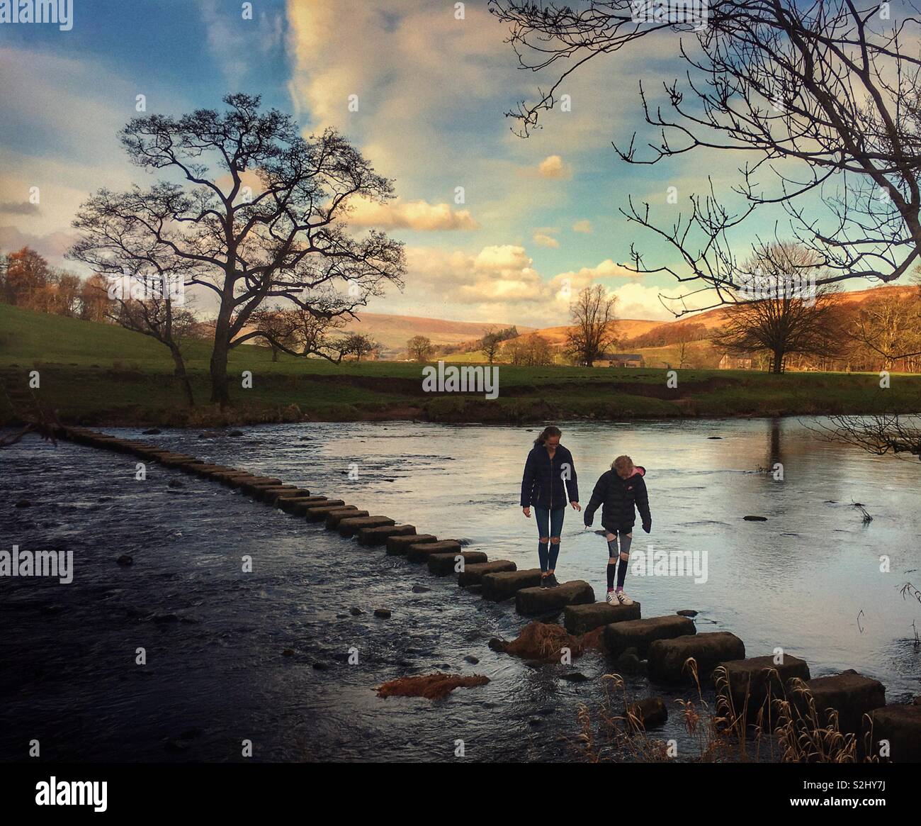 Two girls walking across stepping stones at Whitewell - Smartphone Captured Stock Image
