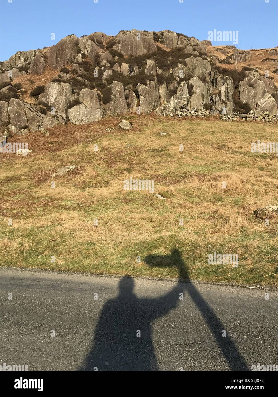 The shadow of a walker resting on a finger post direction sign while walking in the Duden Valley in The English Lake District, Cumbria. Stock Photo