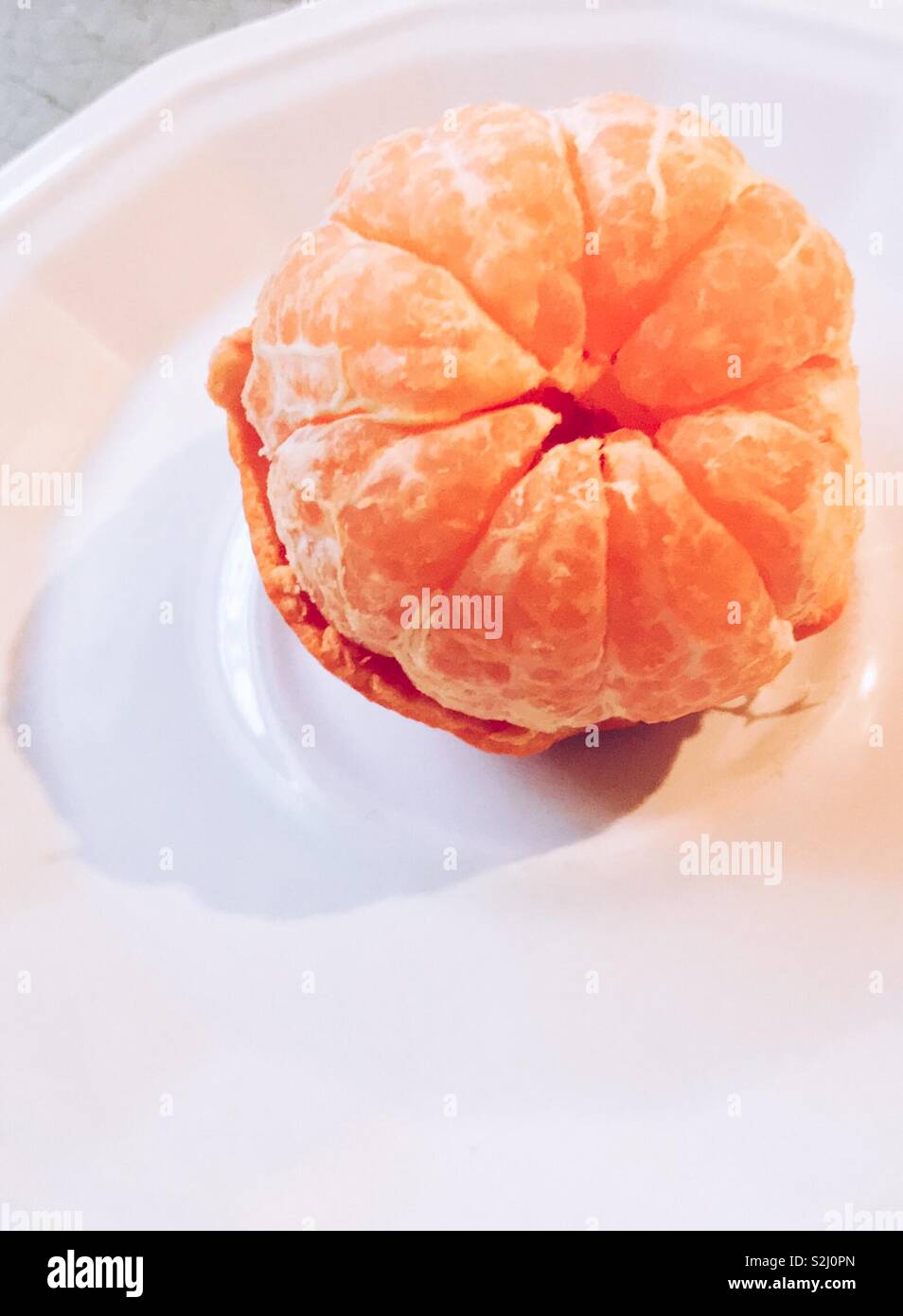 White plate is background for tangerine sections sitting in half of the peeling Stock Photo