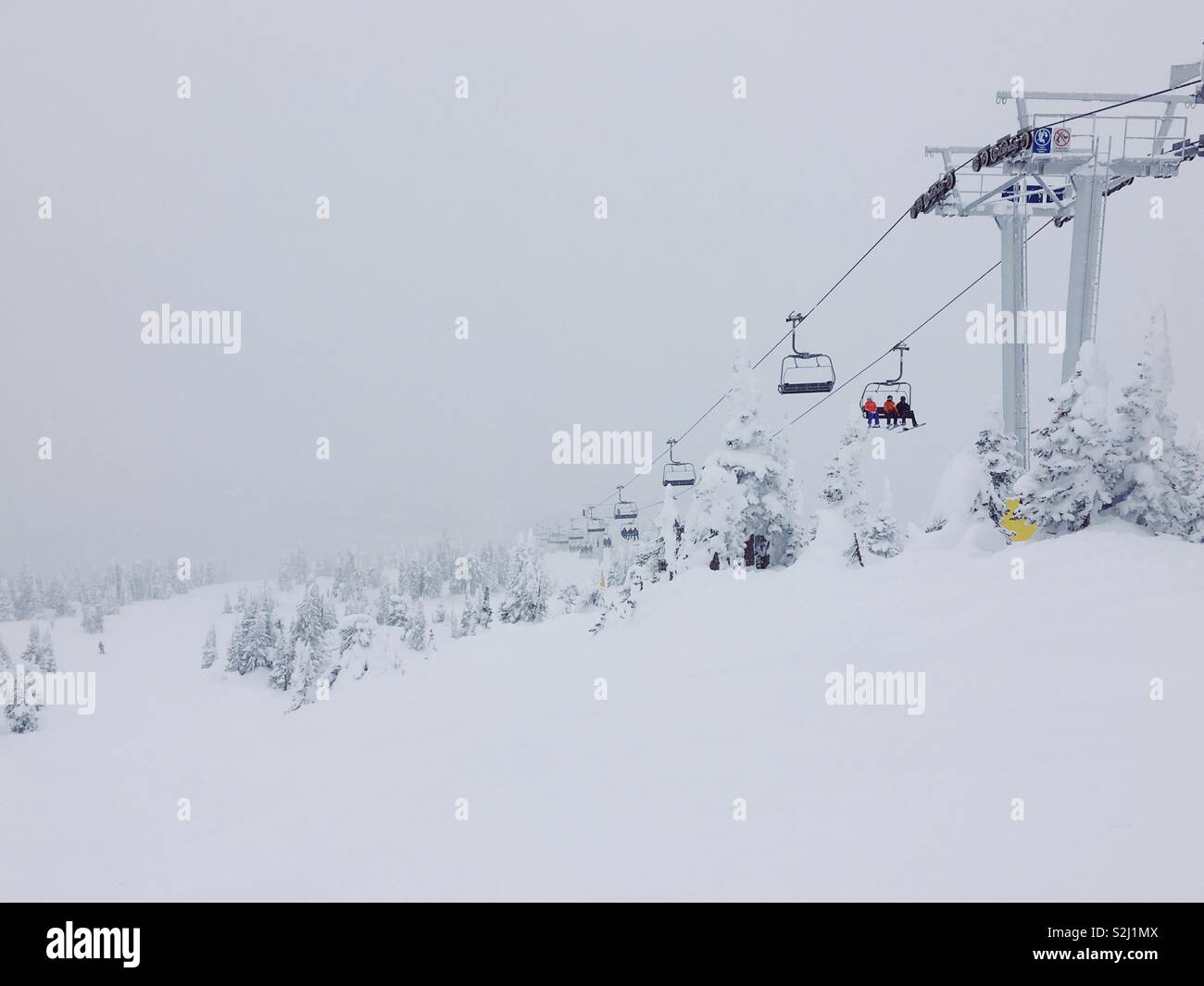 Overcast snowy day on the ski hill, with people on quad chair lift. Space for text. - Smartphone Captured Stock Image