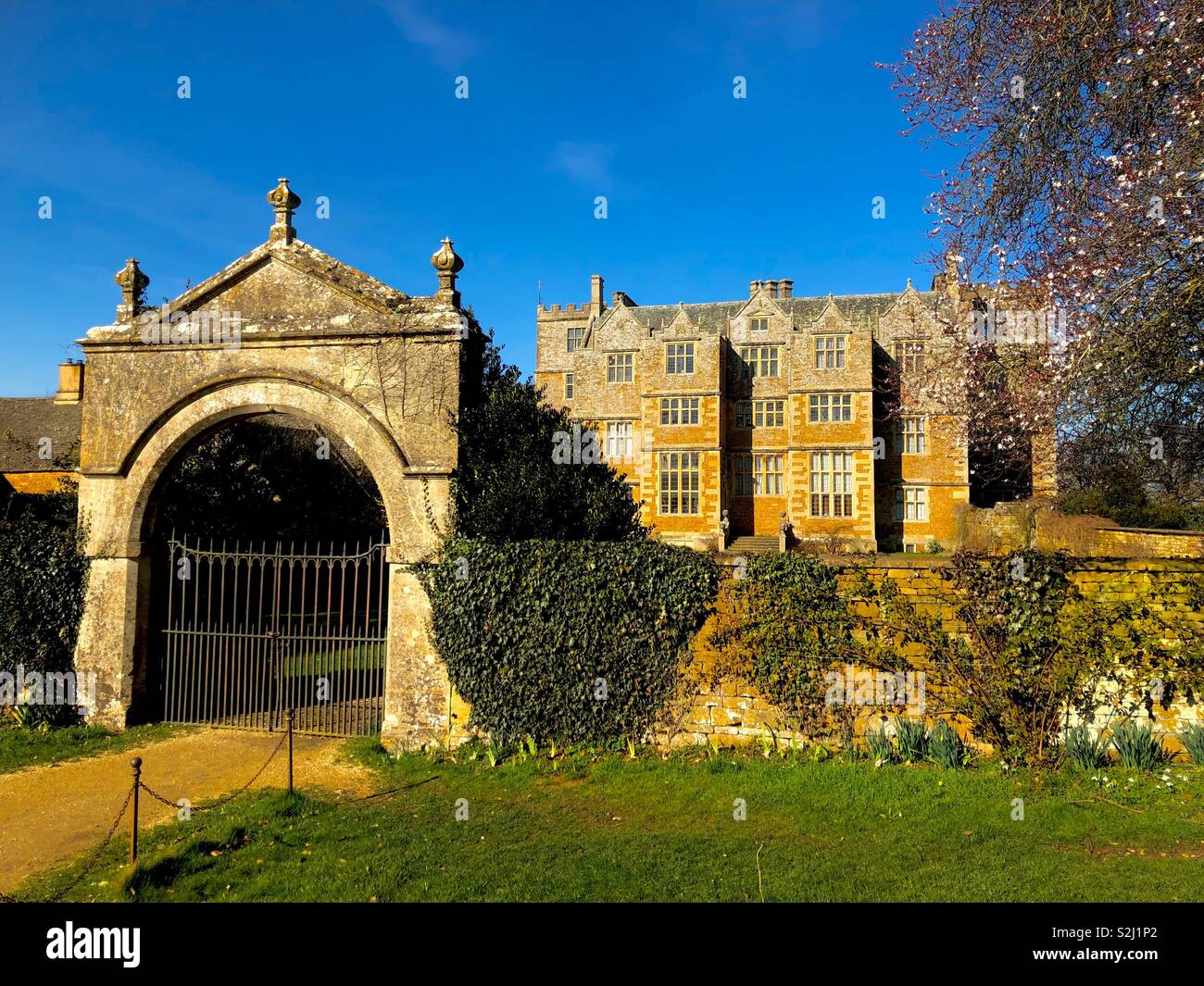 Chastleton Manor and entrance arch brilliantly lit against a deep blue sky on a Spring morning. - Smartphone Captured Stock Image