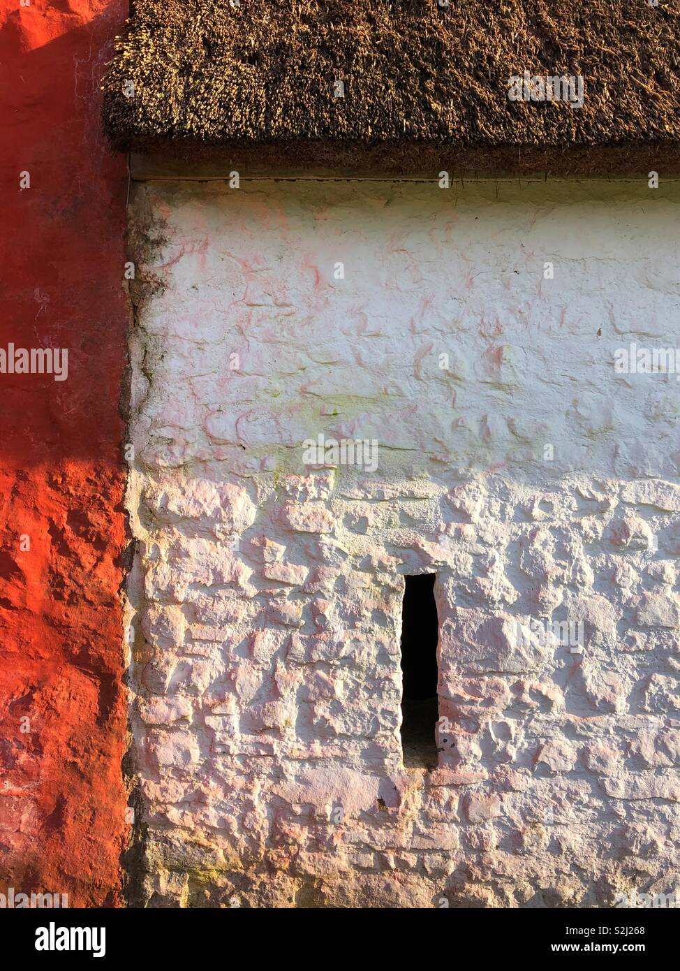 Building detail of whitewashed thatched cottage with a window slit next to a red cottage at the St Fagans Museum of Welsh Life. - Smartphone Captured Stock Image