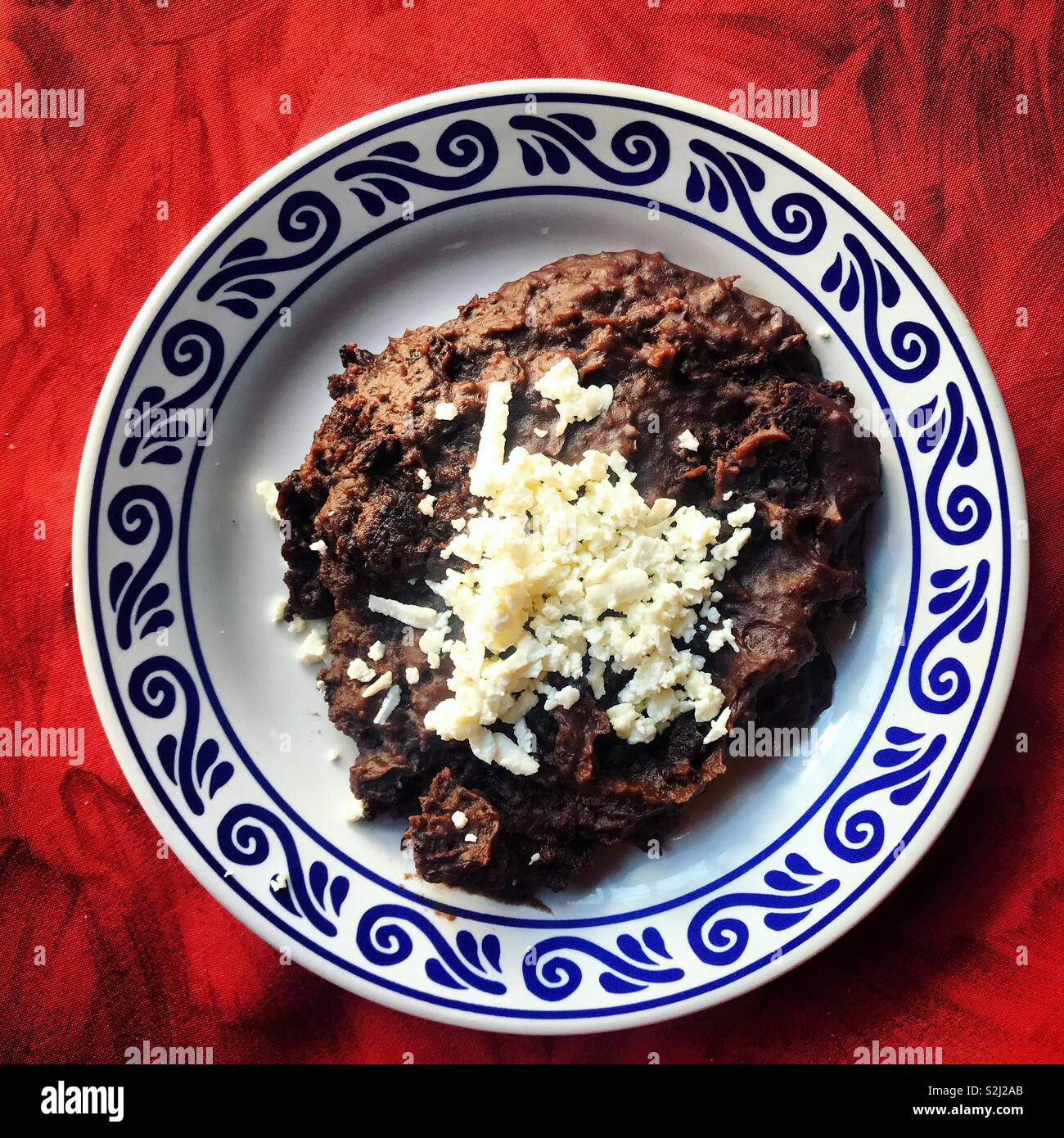 Black beans with cheese in a “talavera” ceramic plate on a red table in Santa Clara restaurant in Puebla, Mexico Stock Photo