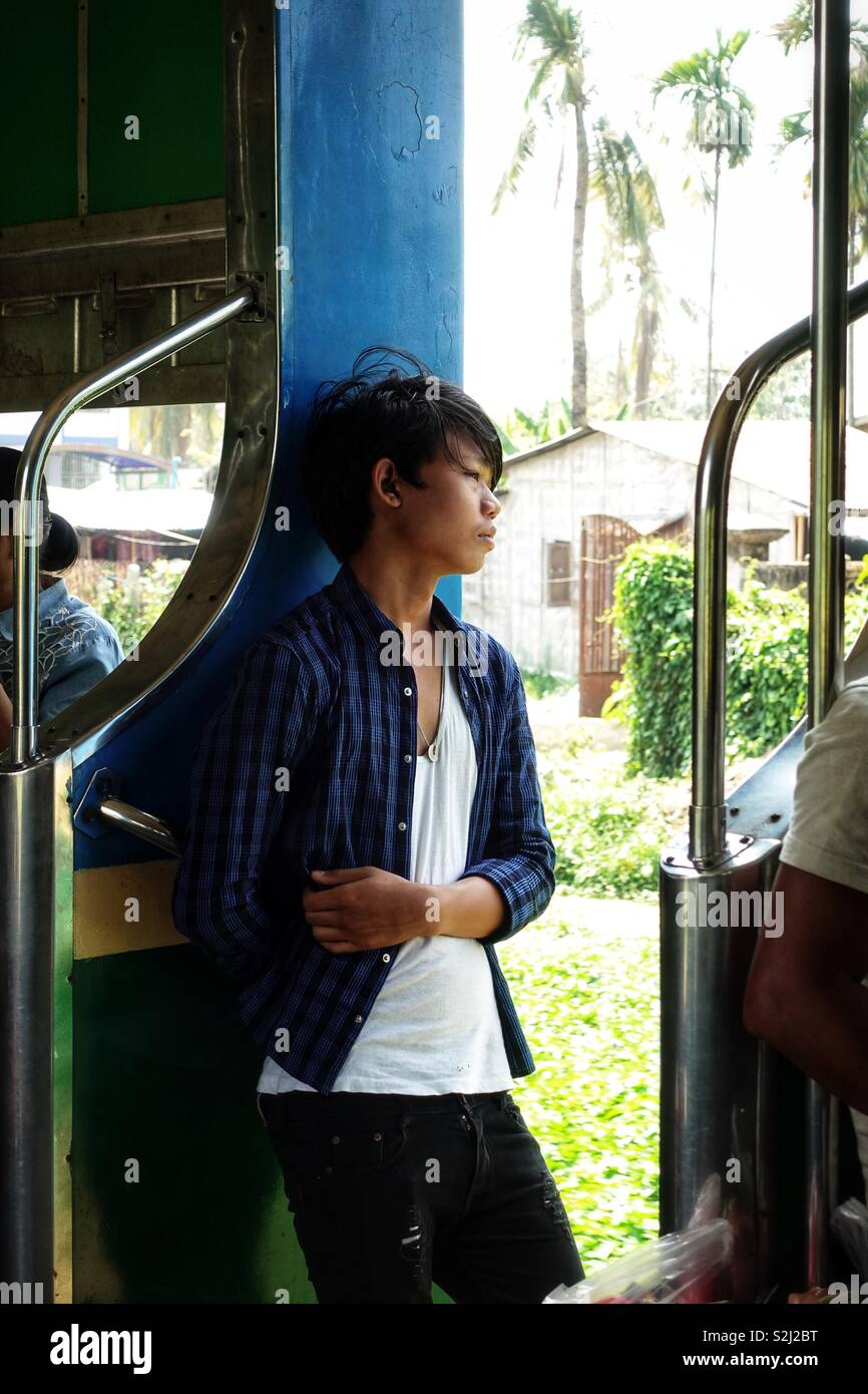 Young burmese boy in a train. Standing in the open door looking into the wind Stock Photo