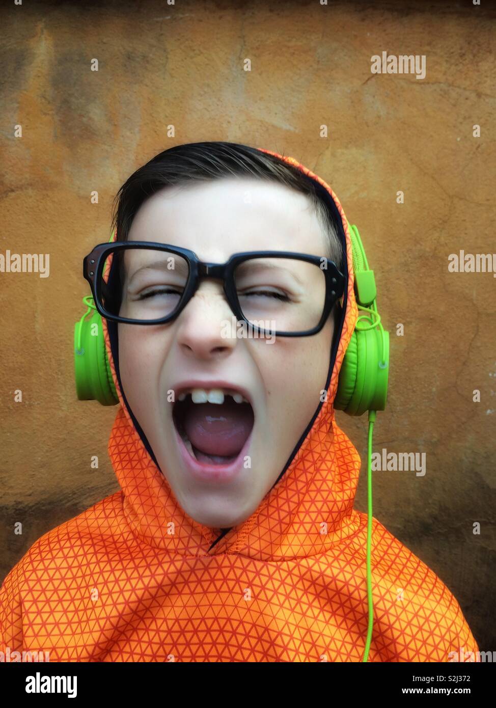 Young boy with black glasses listening and singing to music on stereo headphones Stock Photo