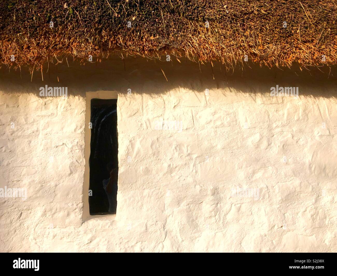 Single window slit in the wall of an old white washed thatched cottage. - Smartphone Captured Stock Image