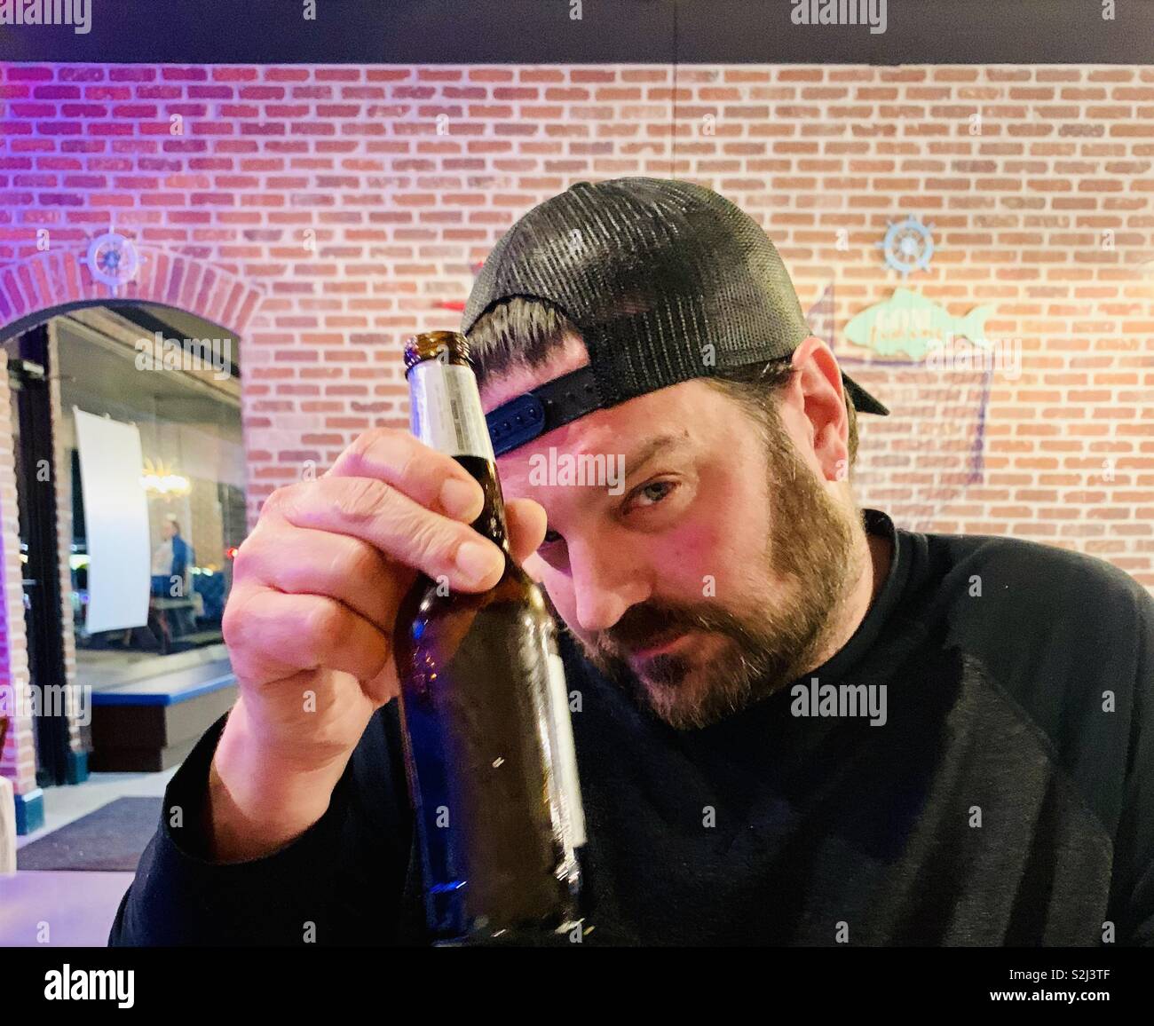 Man holding a beer up in a restaurant to cheers and looking at camera. - Smartphone Captured Stock Image