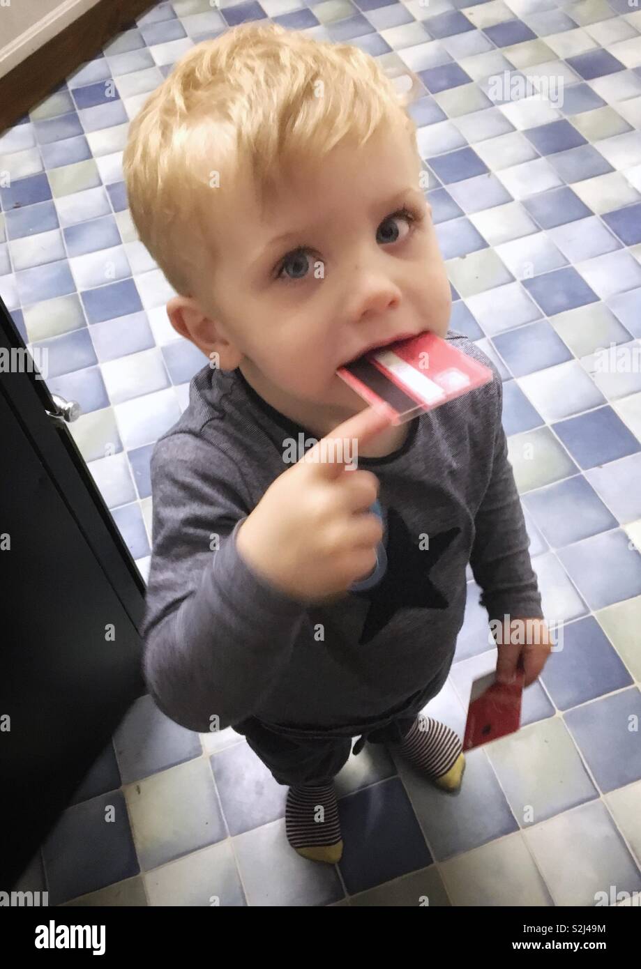 Two year old boy playing with a credit card in his mouth. - Smartphone Captured Stock Image