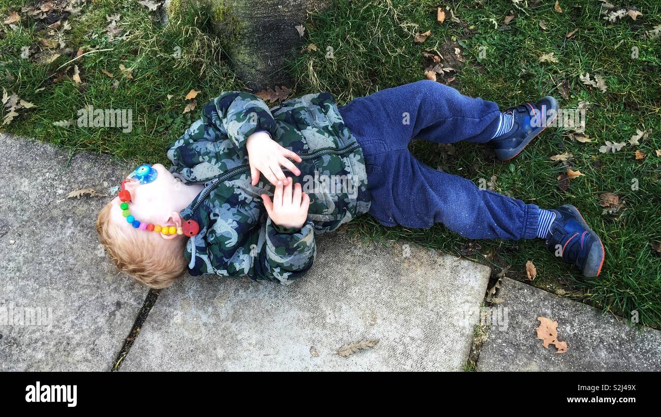 Exhausted two year old boy sleeping outside on the ground Stock Photo